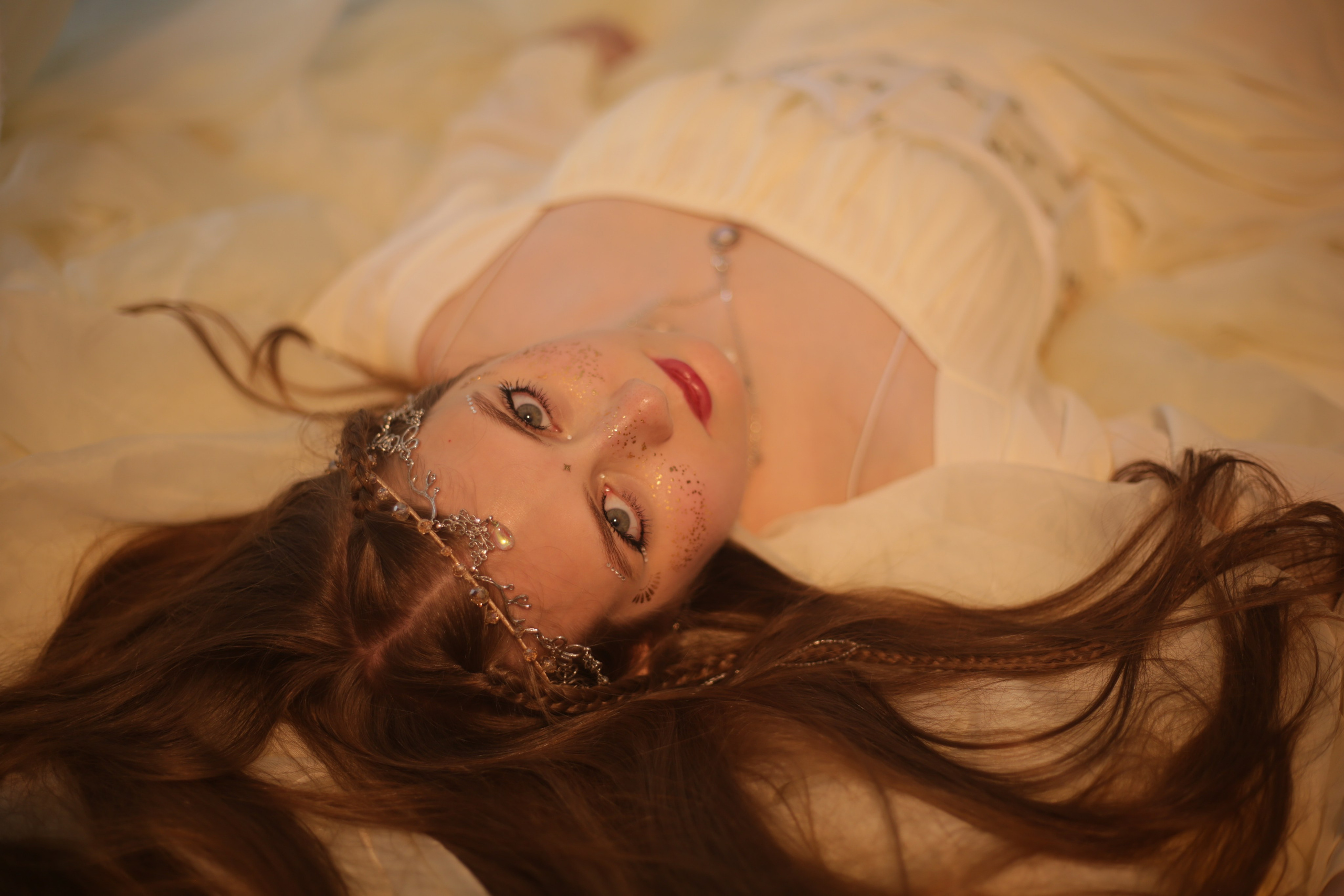 Фотография эльфийки в Перми: девушка в белом платье лежит на кровати под балдахином среди цветов и свечей