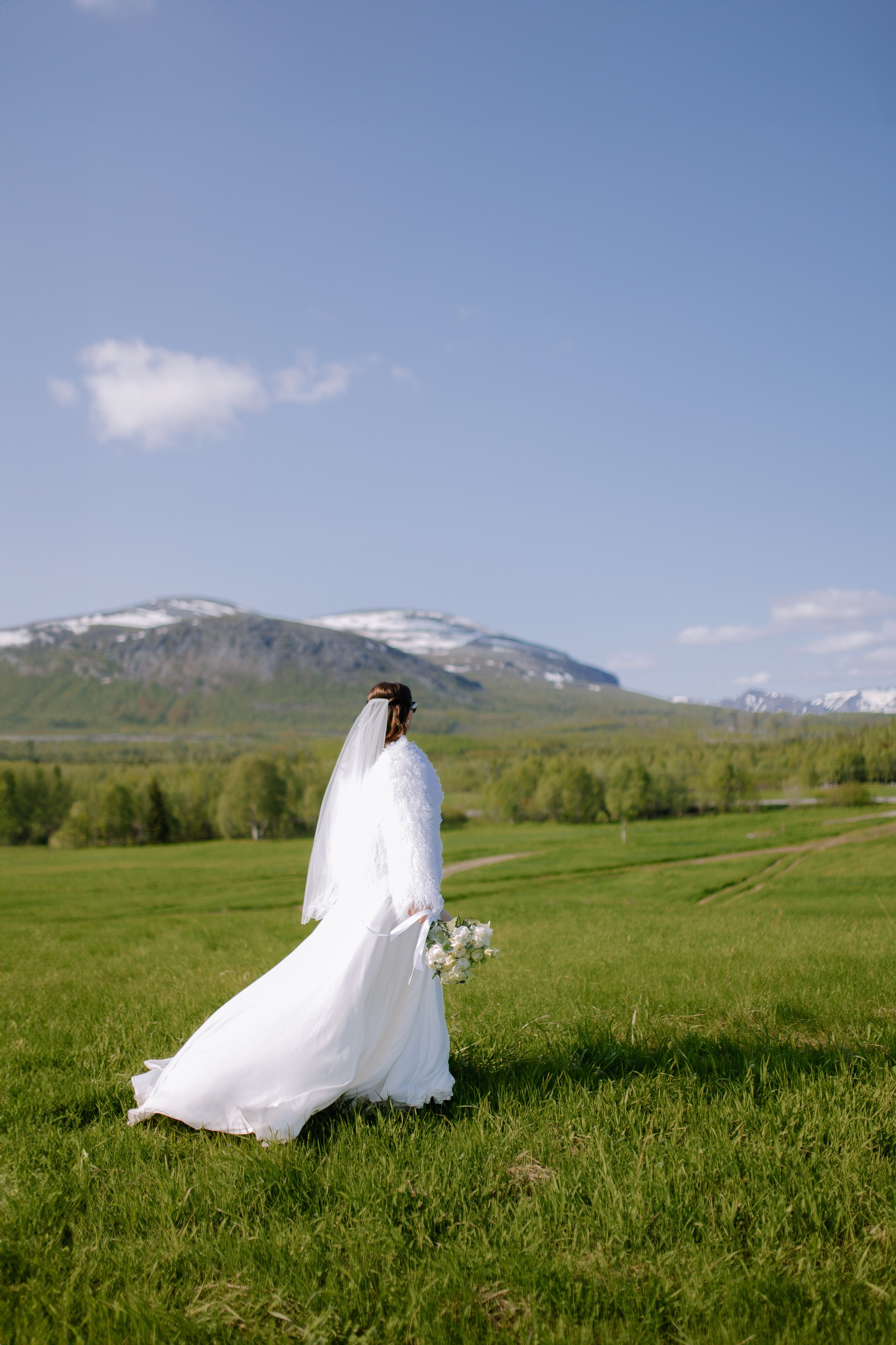 Девушка в элегантном свадебном платье идёт среди величественных горных вершин.