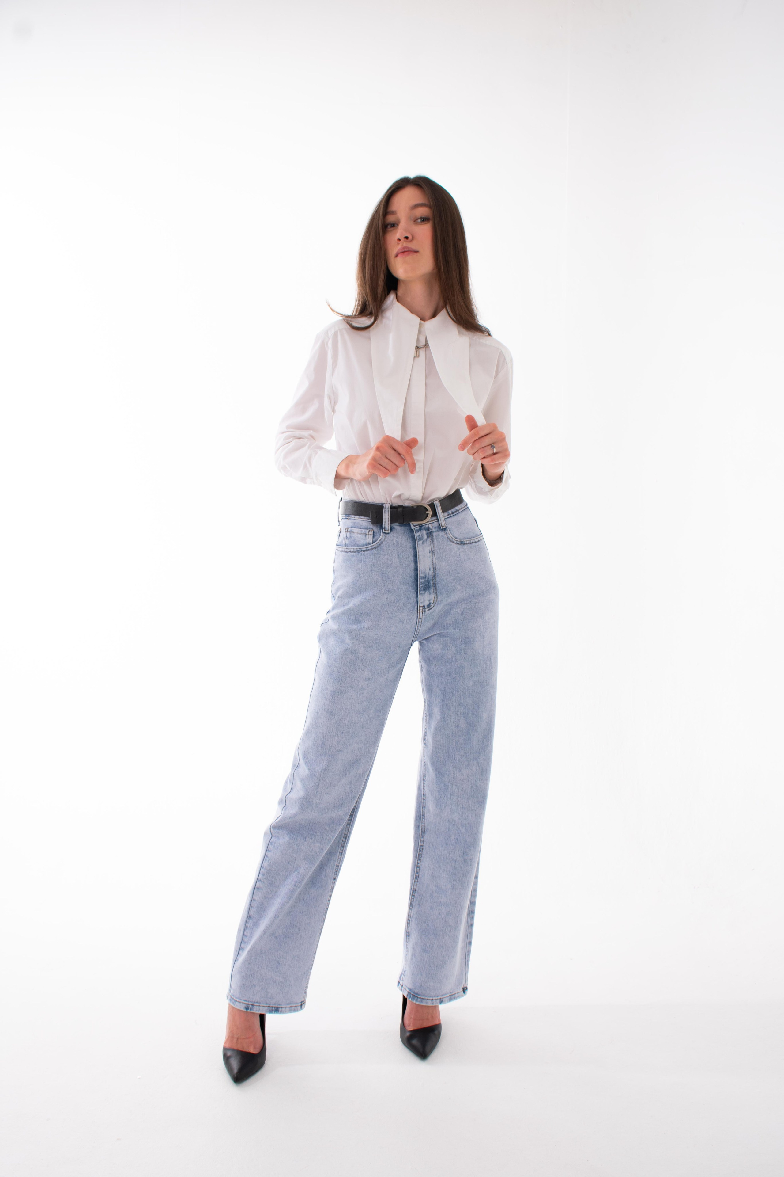 Модель фотографируется в студии в белой рубашке и джинсах