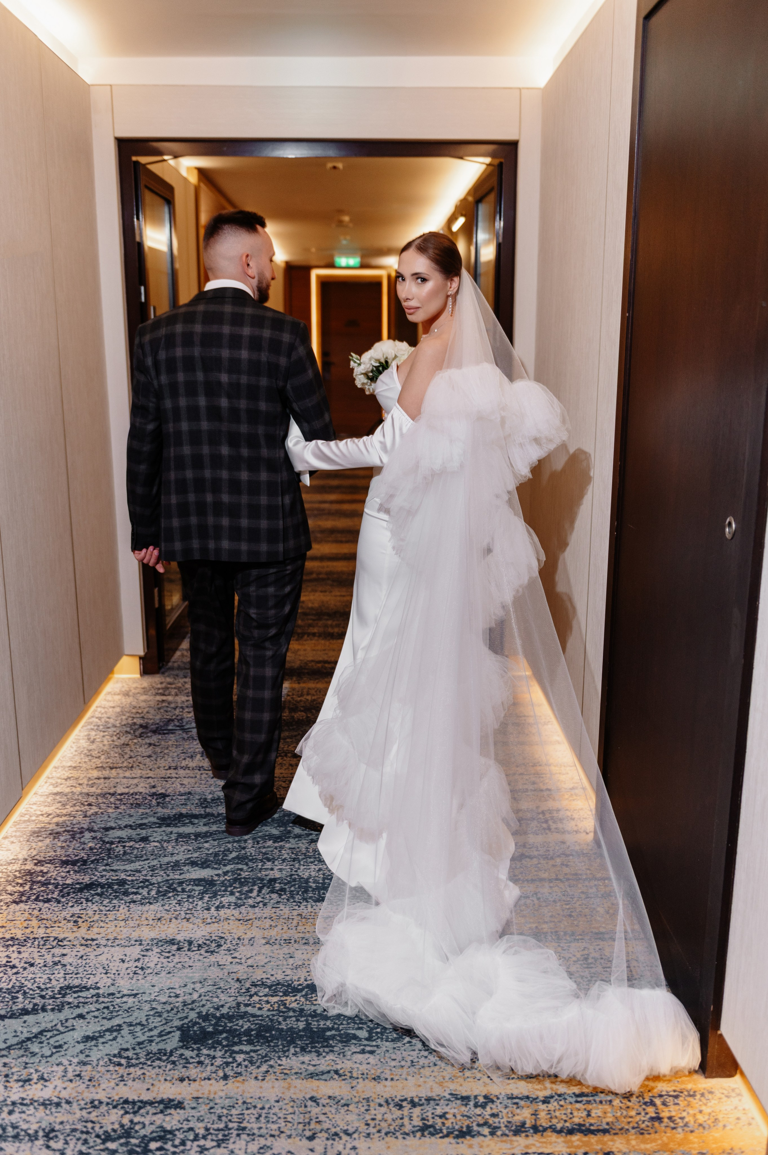 Молодожены идут по коридору отеля под ручку.
