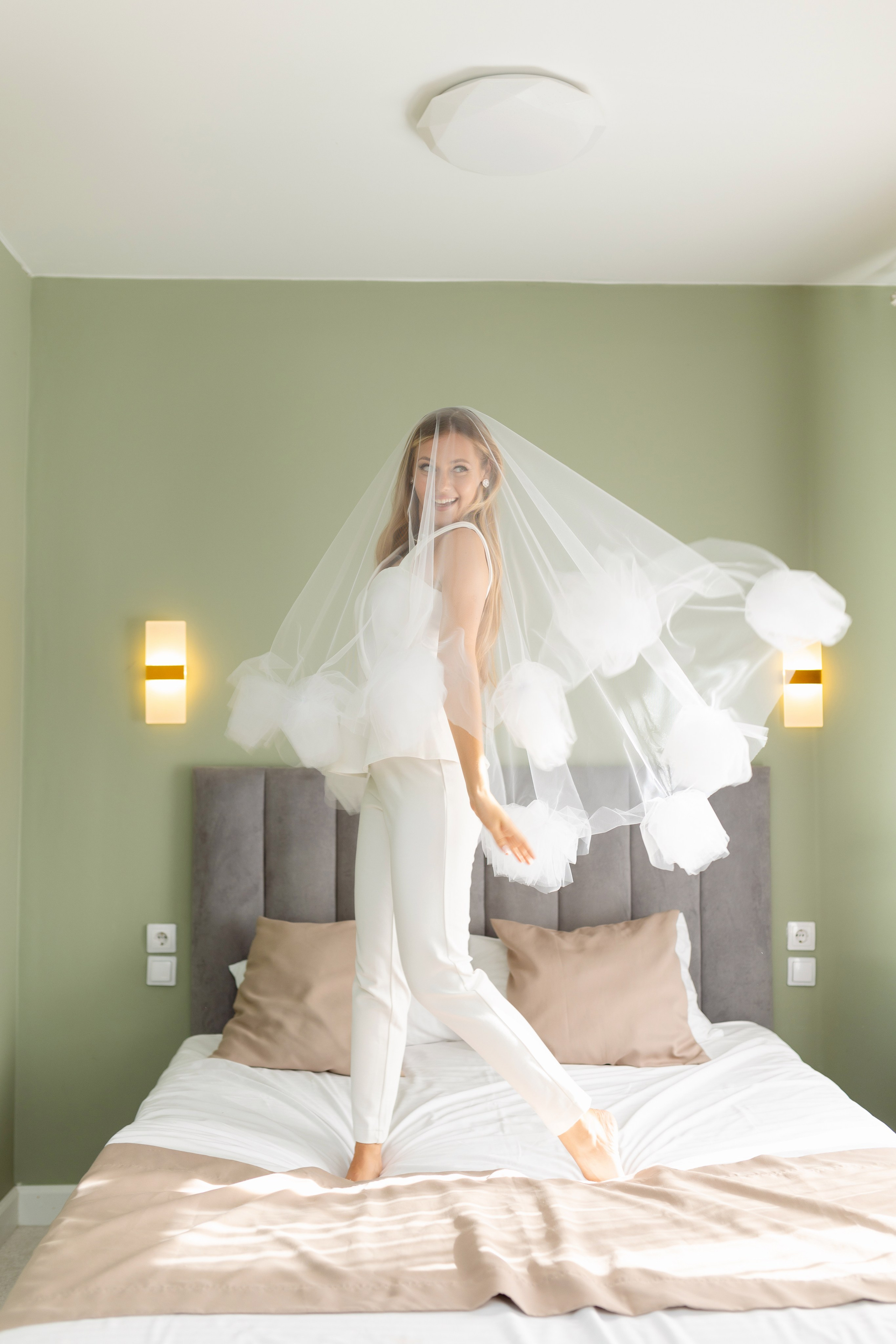 Невеста стоит на кровати. вокруг нее развивается вуаль.