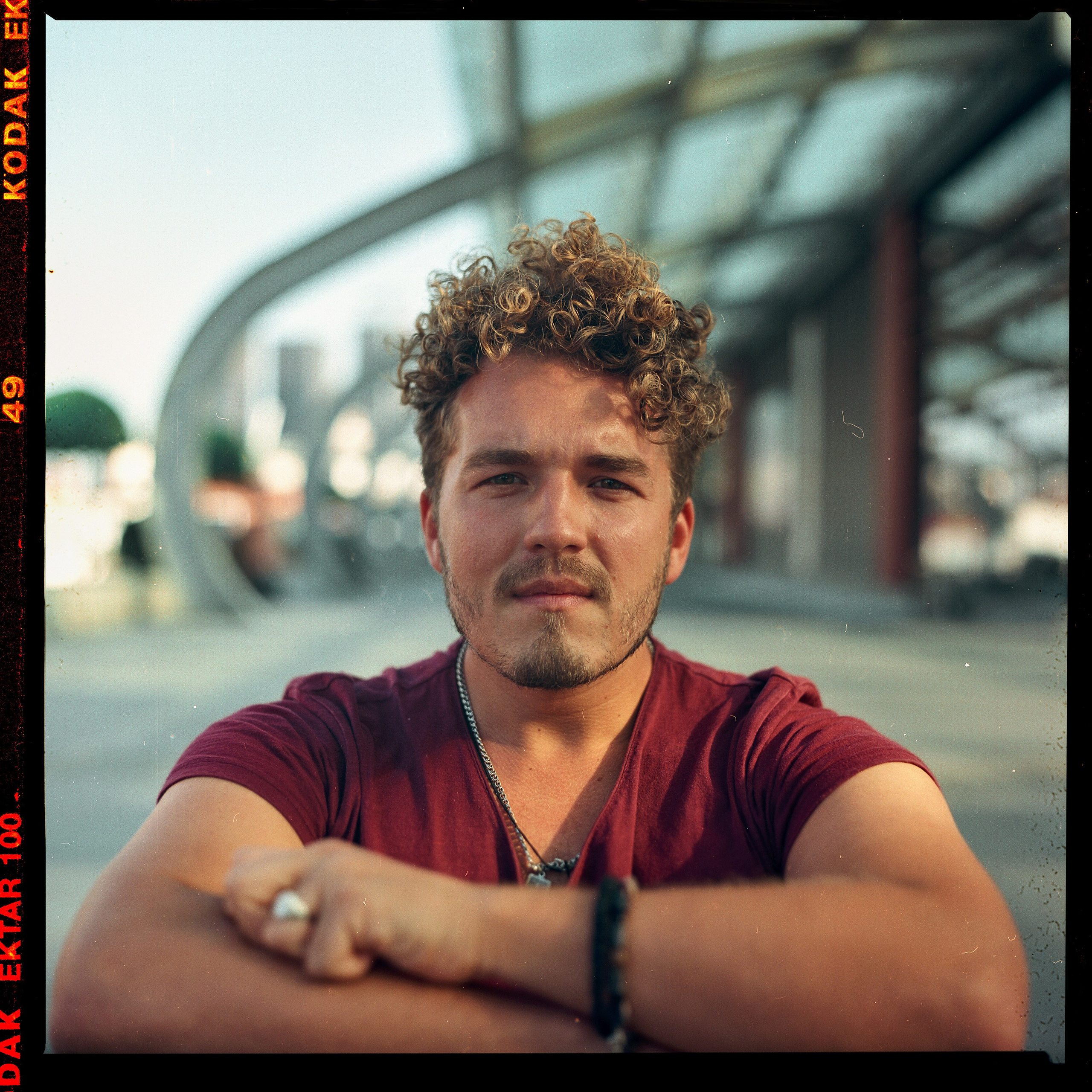 Кучерявый молодой человек сидит на фоне вокзала в Харбине 