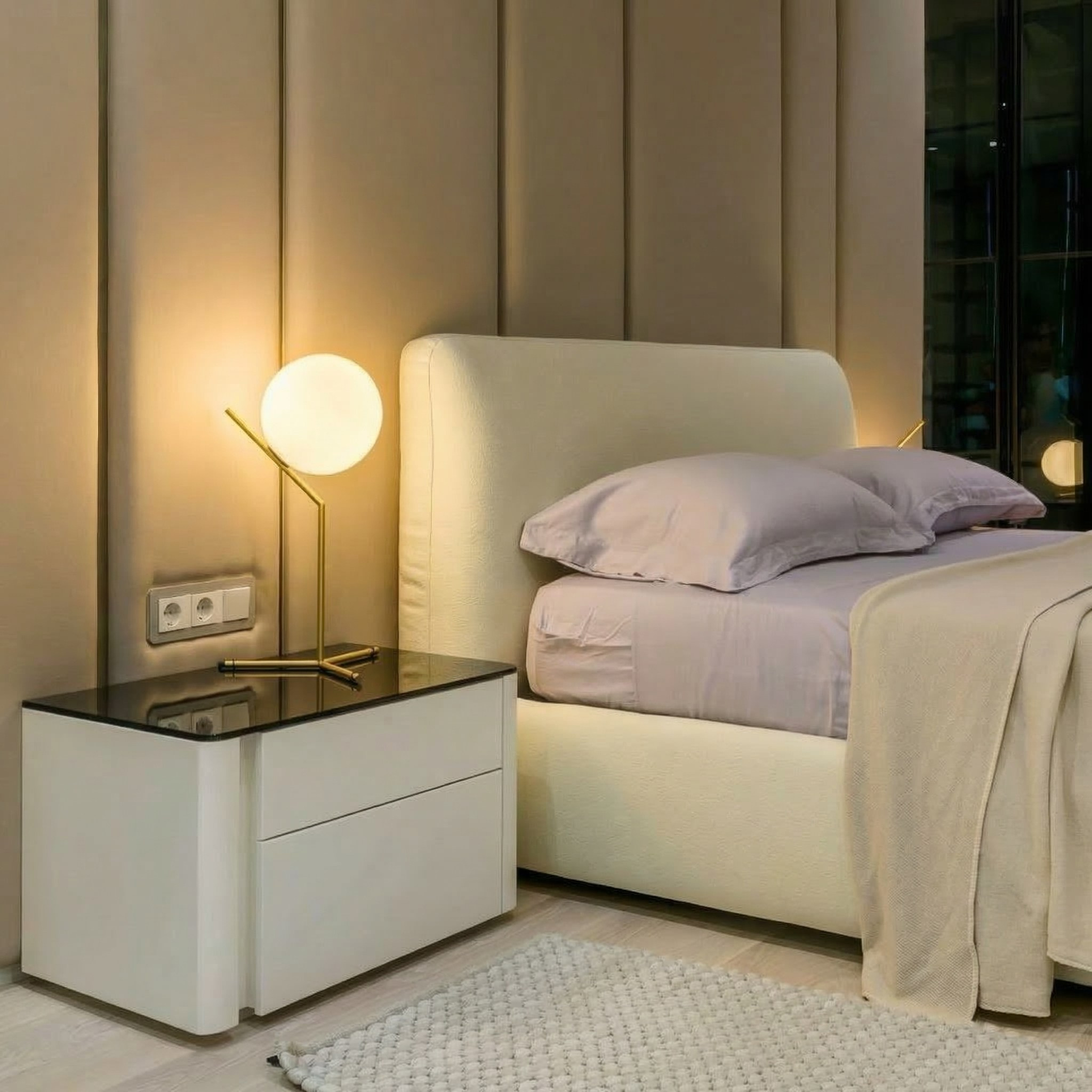 Детали интерьера спальни 118 кв.м: современная белая прикроватная тумба с черным стеклом, дизайнерский настольный светильник и кровать с высоким мягким изголовьем. Реализованный проект Валерии Котович.