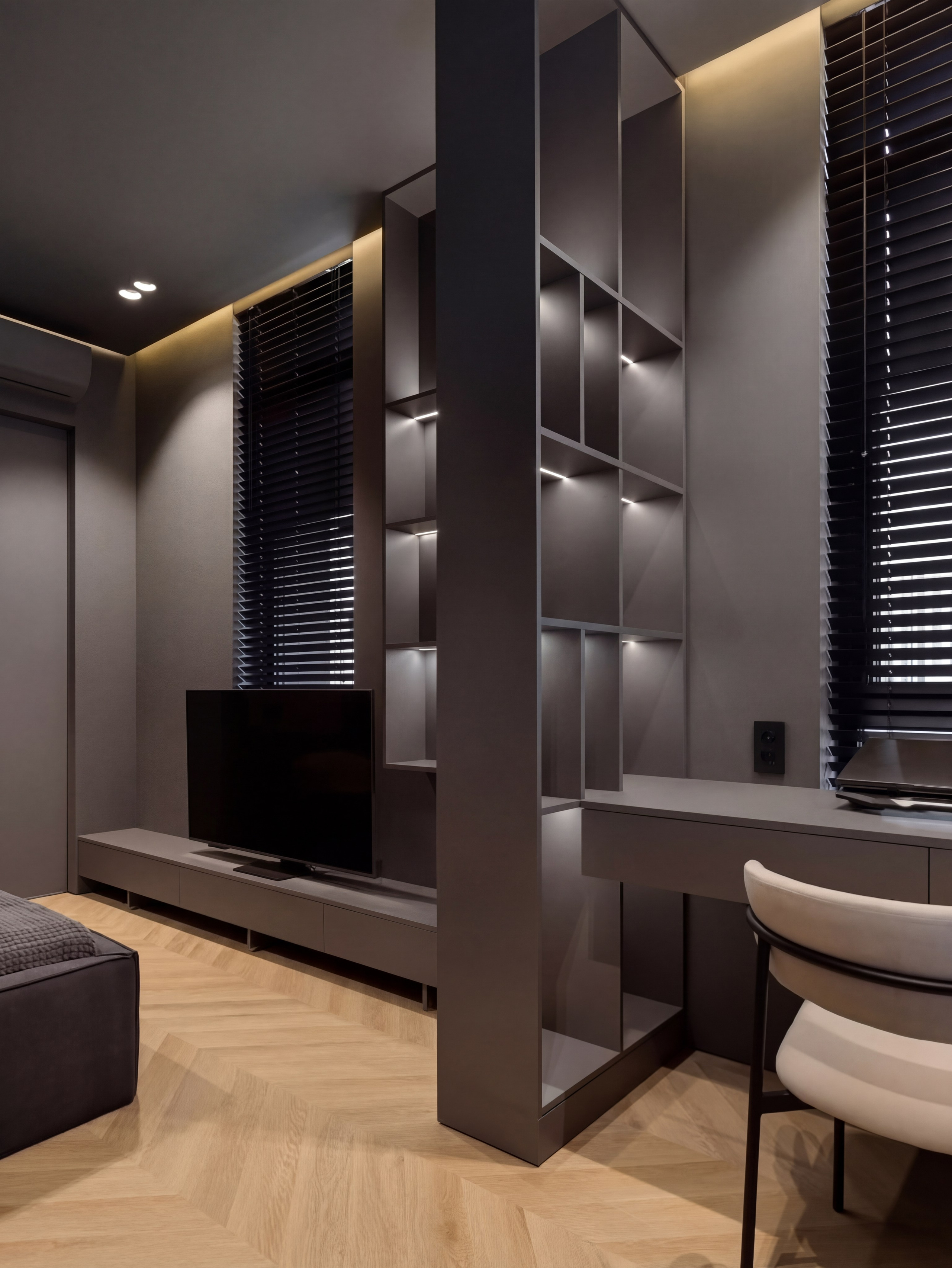 Рабочая зона и ТВ-зона в спальне подростка от Валерии Котович: сквозной стеллаж с подсветкой, лаконичный стол, дизайнерское кресло и паркет елочкой в темно-сером интерьере.