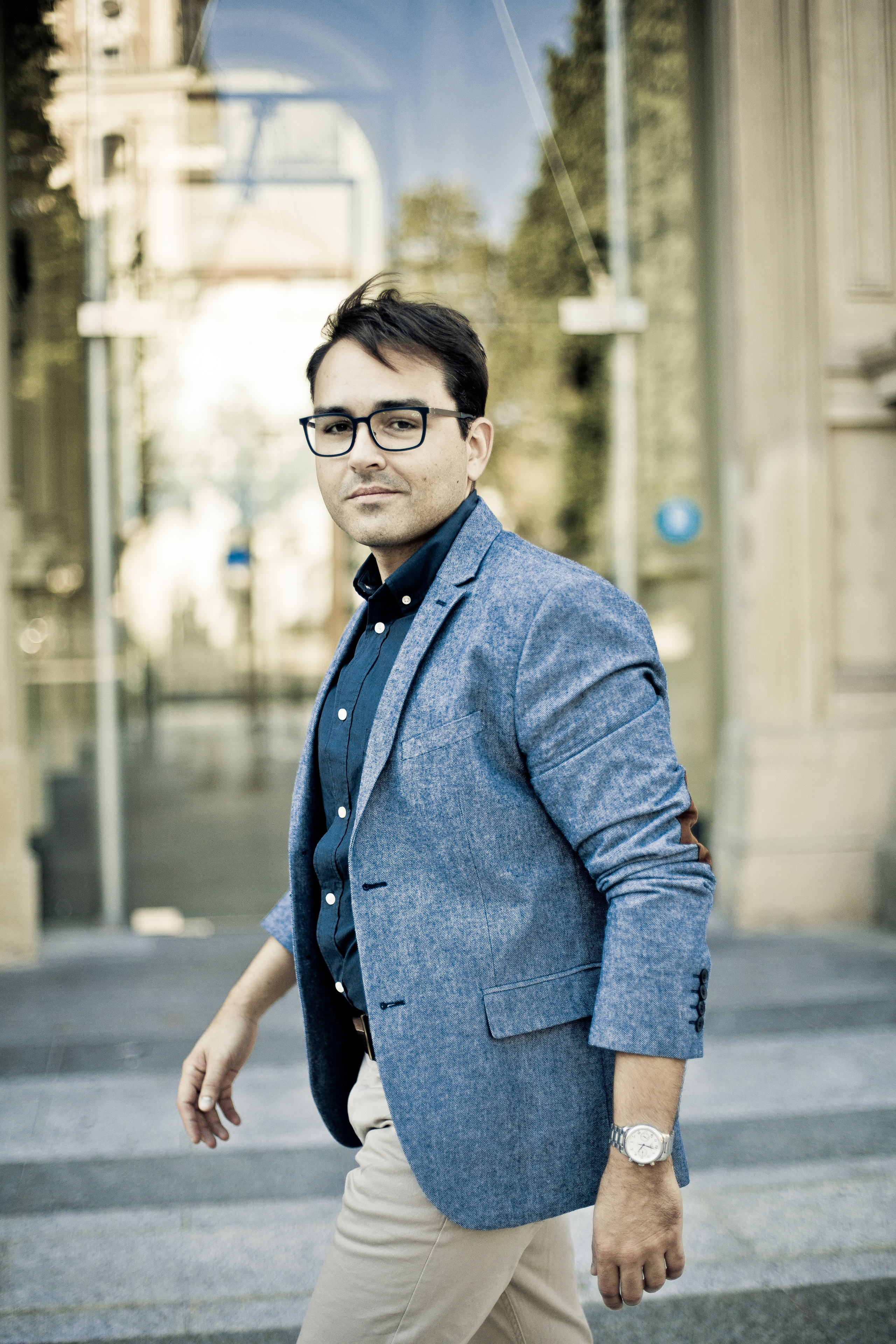 стильный юноша в очках и пиджаке идет по улице