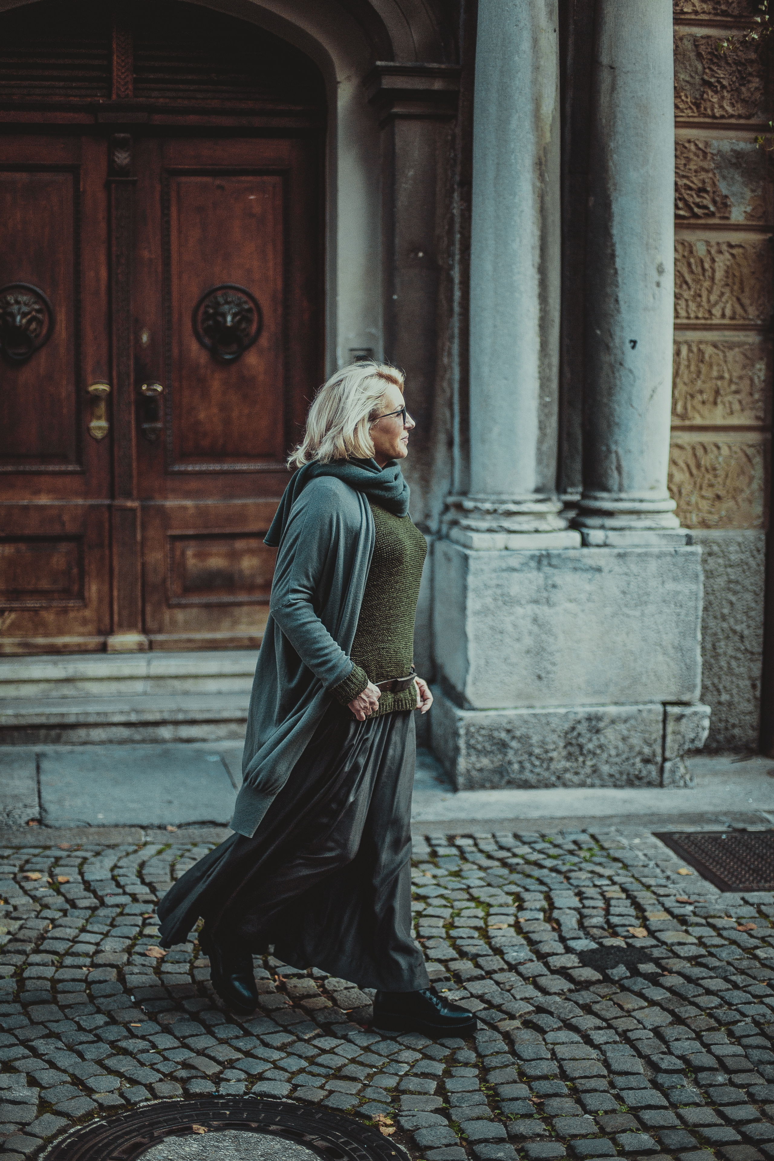 женщина в серо-зеленом идущая по каменной мостовой
