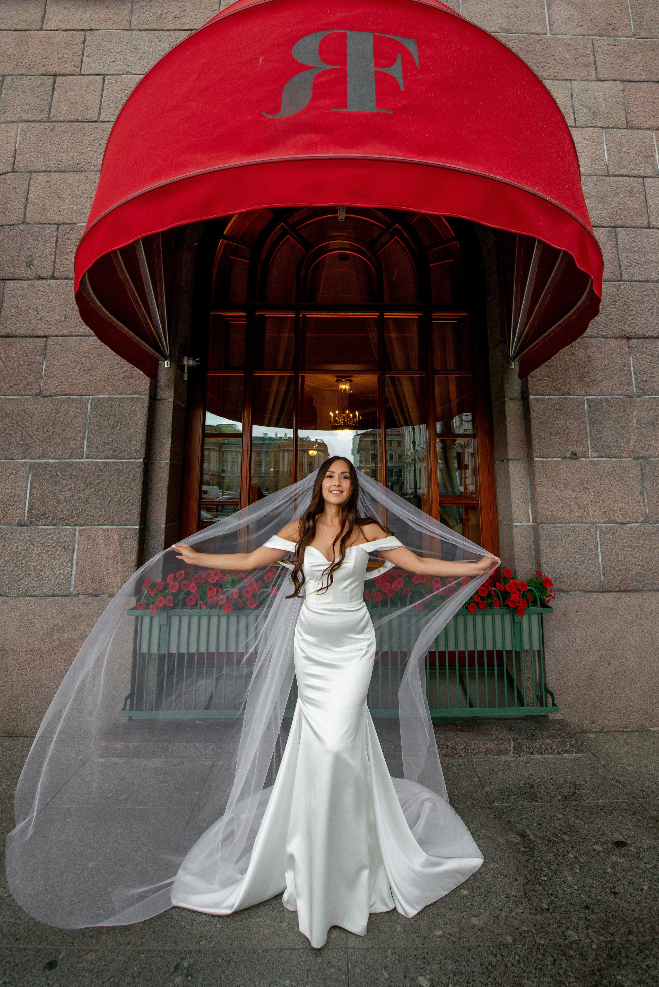 Фотосессия красивой невесты в элегантном платье под красными маркизами гостиницы Астории