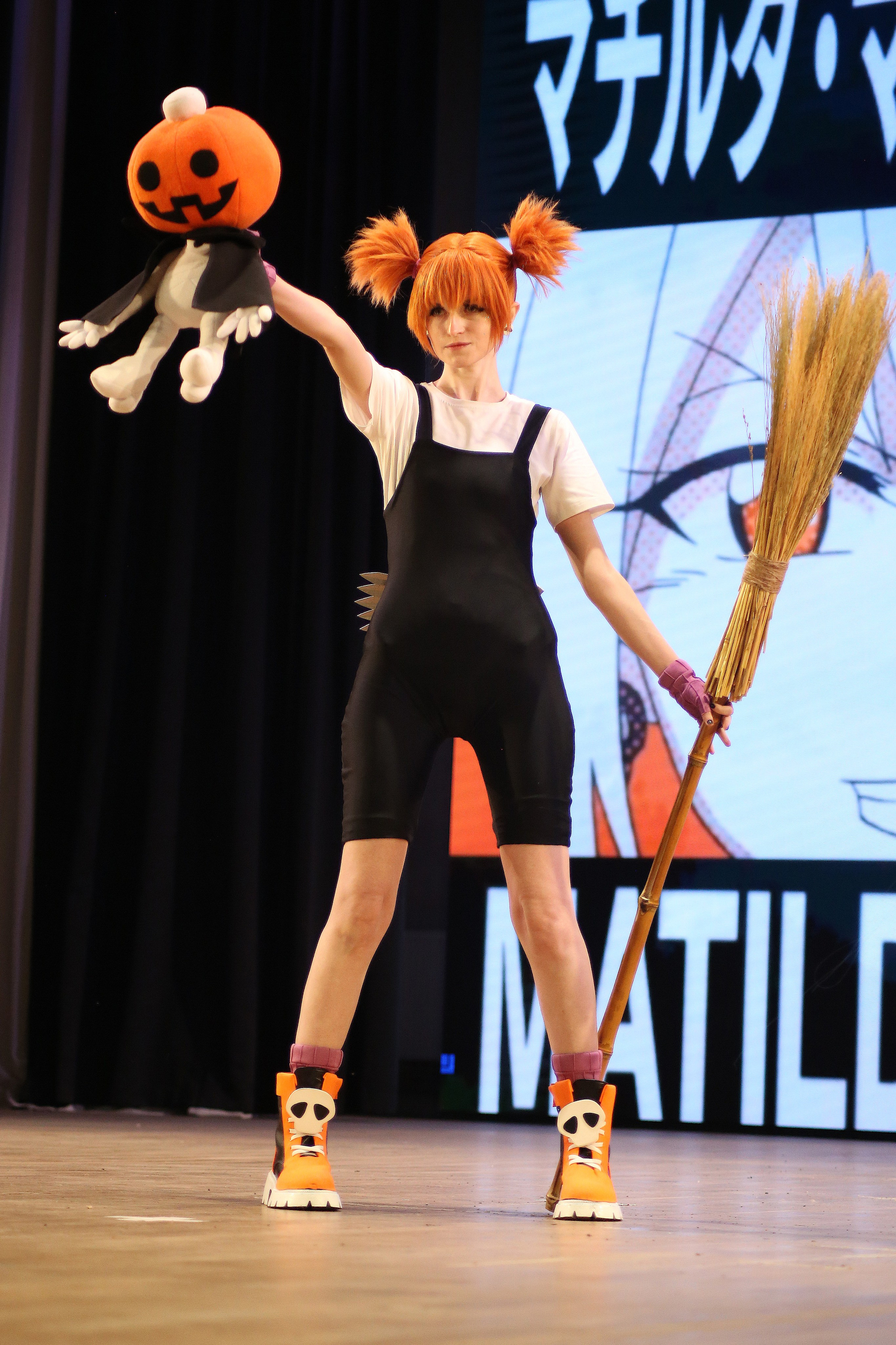 Косплей фотосессия: девушка в черном костюме с метлой и тыквой на сцене