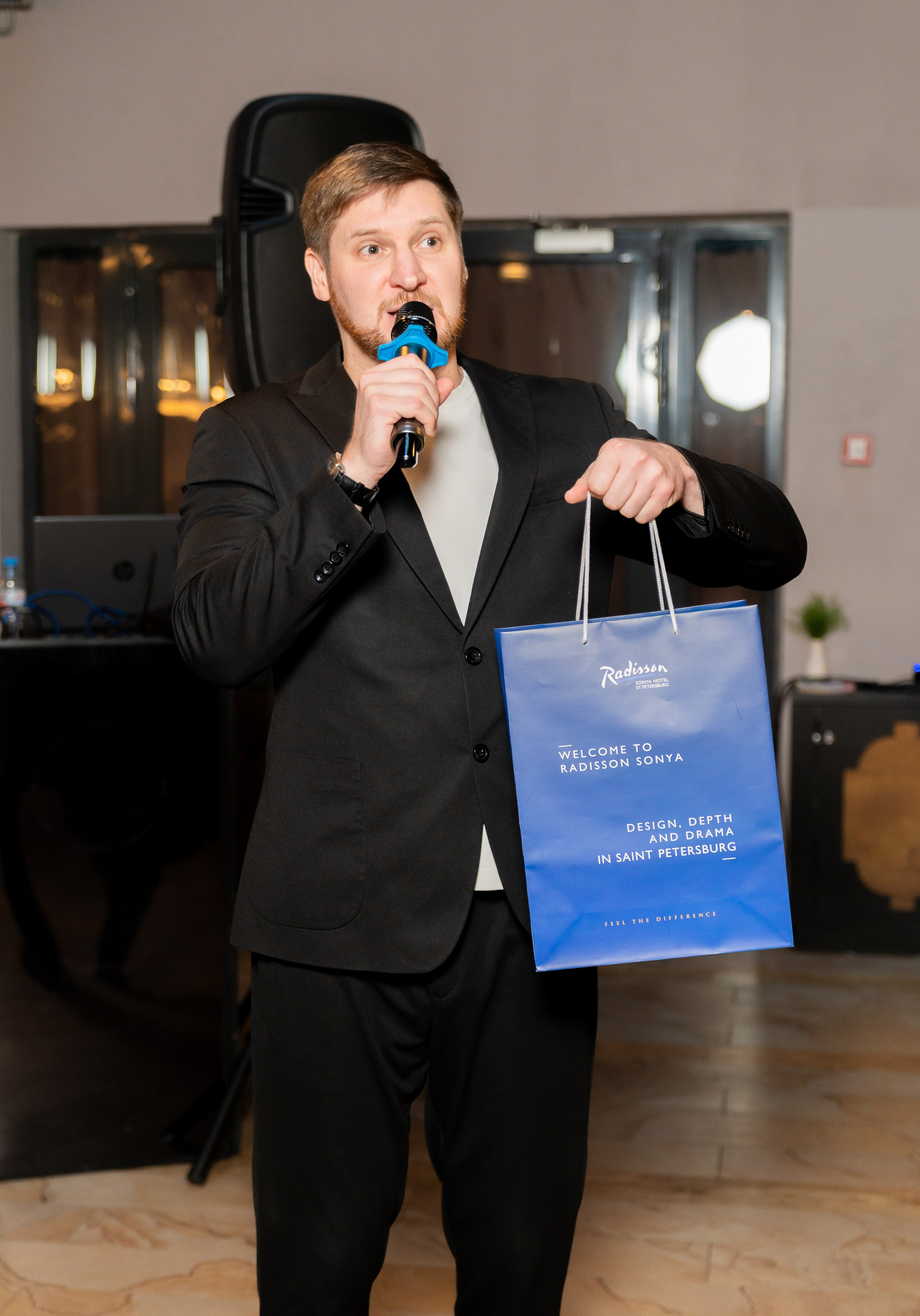 Мужчина-ведущий с микрофоном и синим подарочным пакетом Radisson Sonya. Фото Евгения Мальцева.