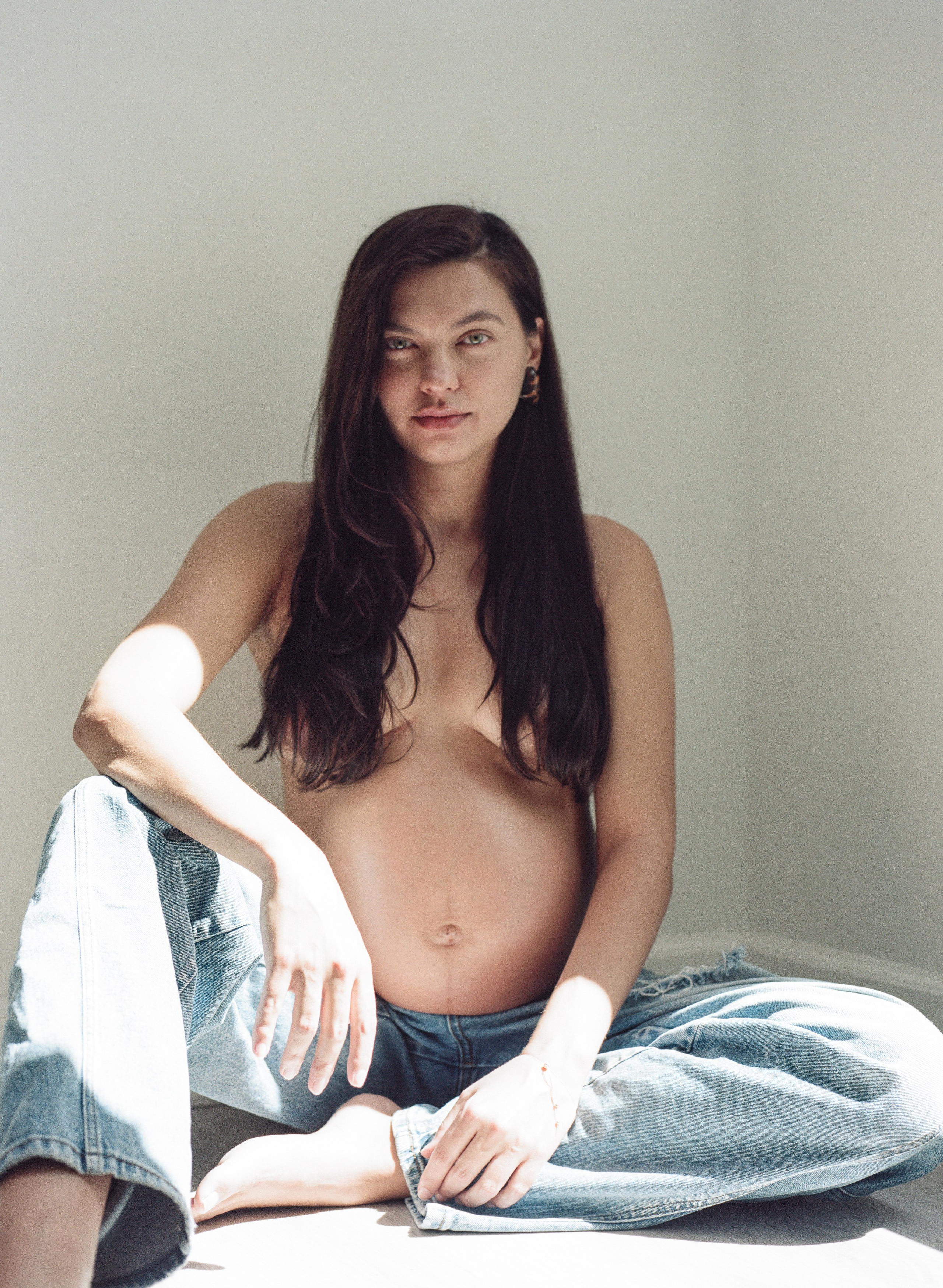A gorgeous expecting woman in jeans sitting on the floor in the studio editorial style film photo