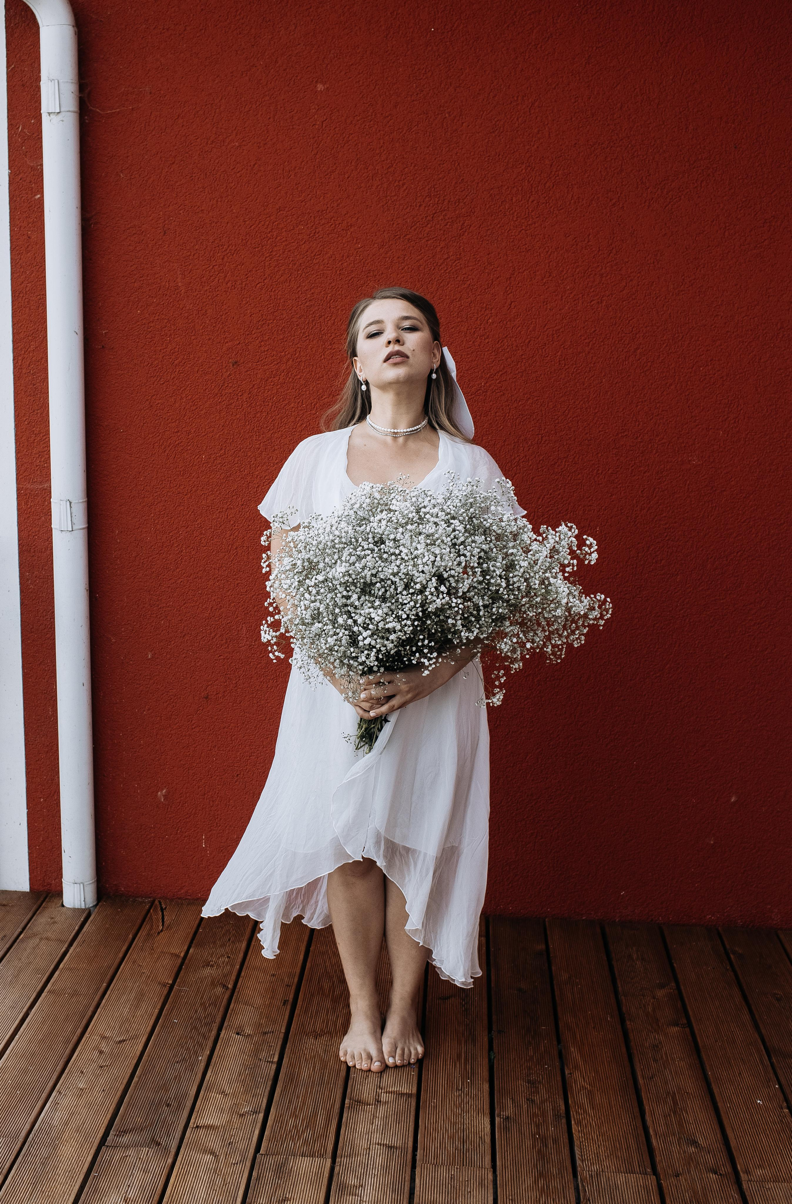Невеста позирует с букетом цветов на фоне красной стены