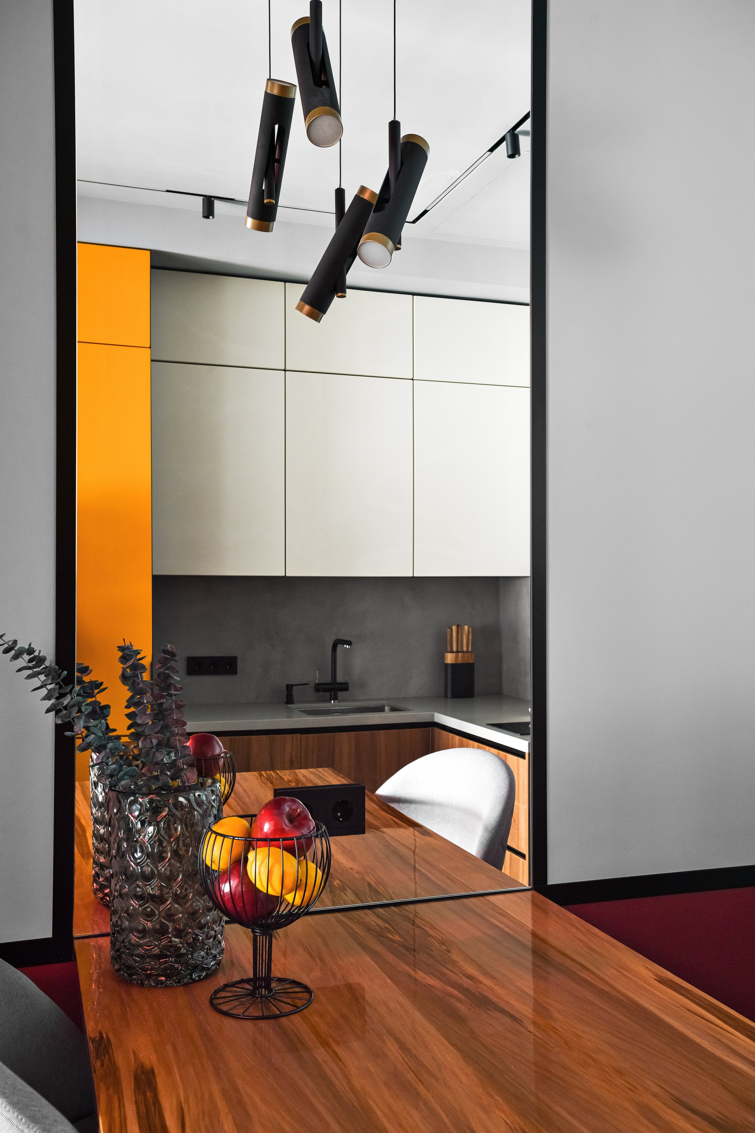 Кухня-столовая: деревянный стол, подвесные светильники, белые фасады и яркий цветовой акцент.