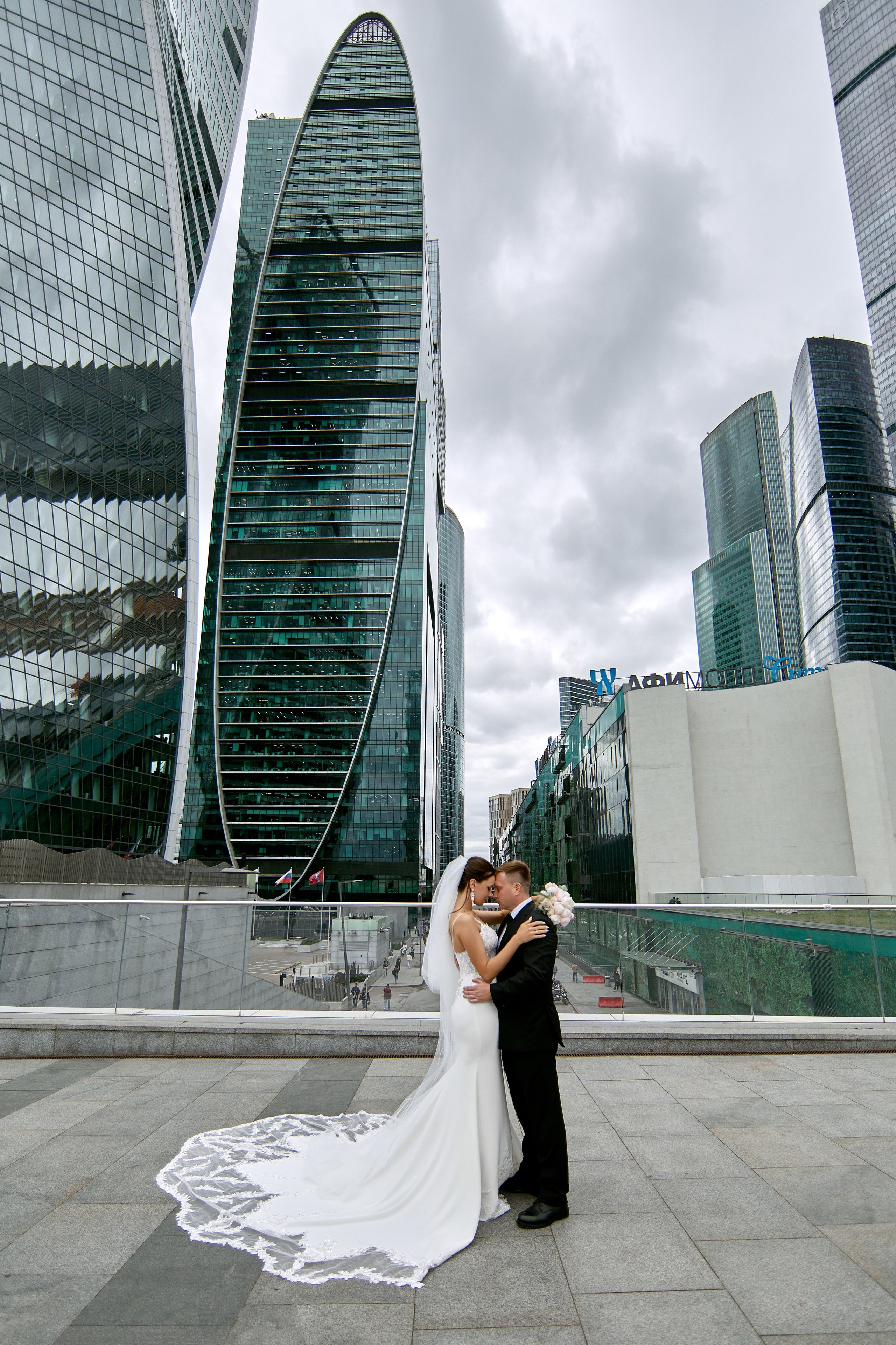 Фотограф свадеб проводит фотосессию для молодоженов в Москва СИТИ – снимок девушки в свадебном платье и мужчины в свадебном костюме на фоне небоскребов