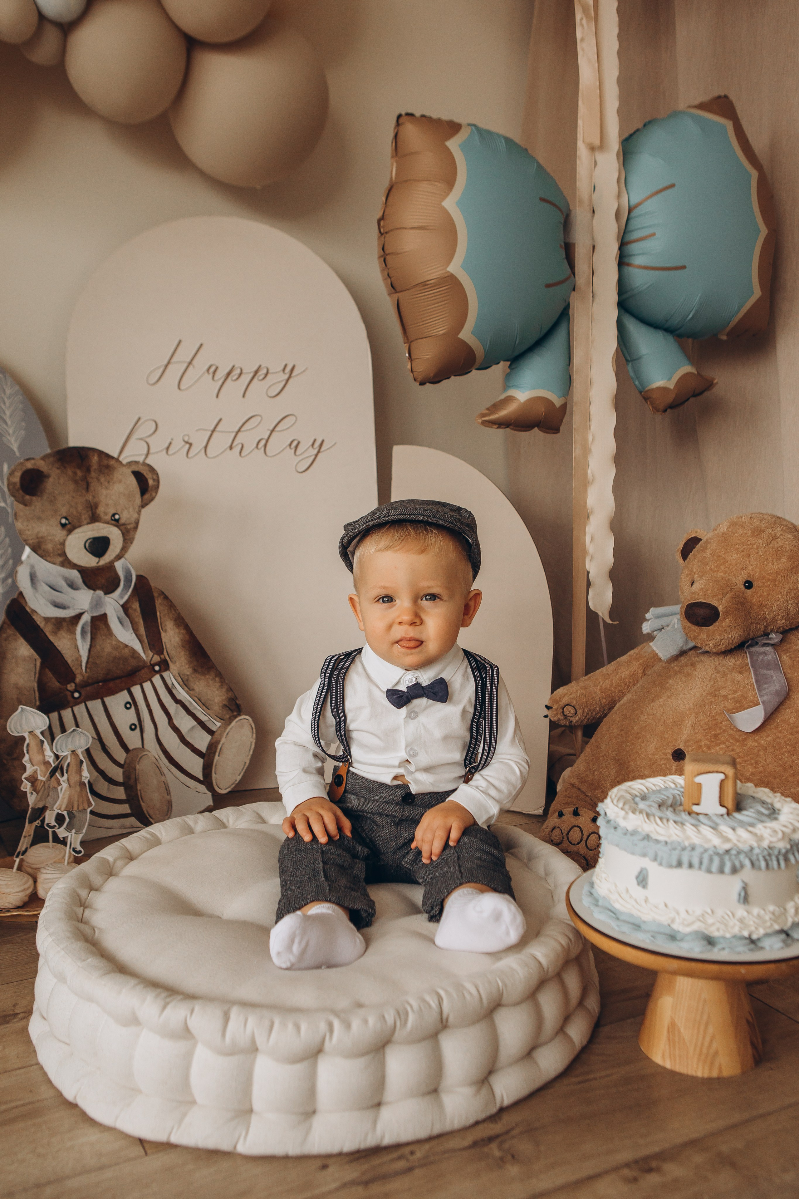 Серьезный маленький мальчик в официальном сером костюме, белой рубашке, кепке и с бабочкой позирует в свой день рождения. Фотосессии детских праздников в Санкт-Петербурге, детский и семейный фотограф Маруся Самылкина.