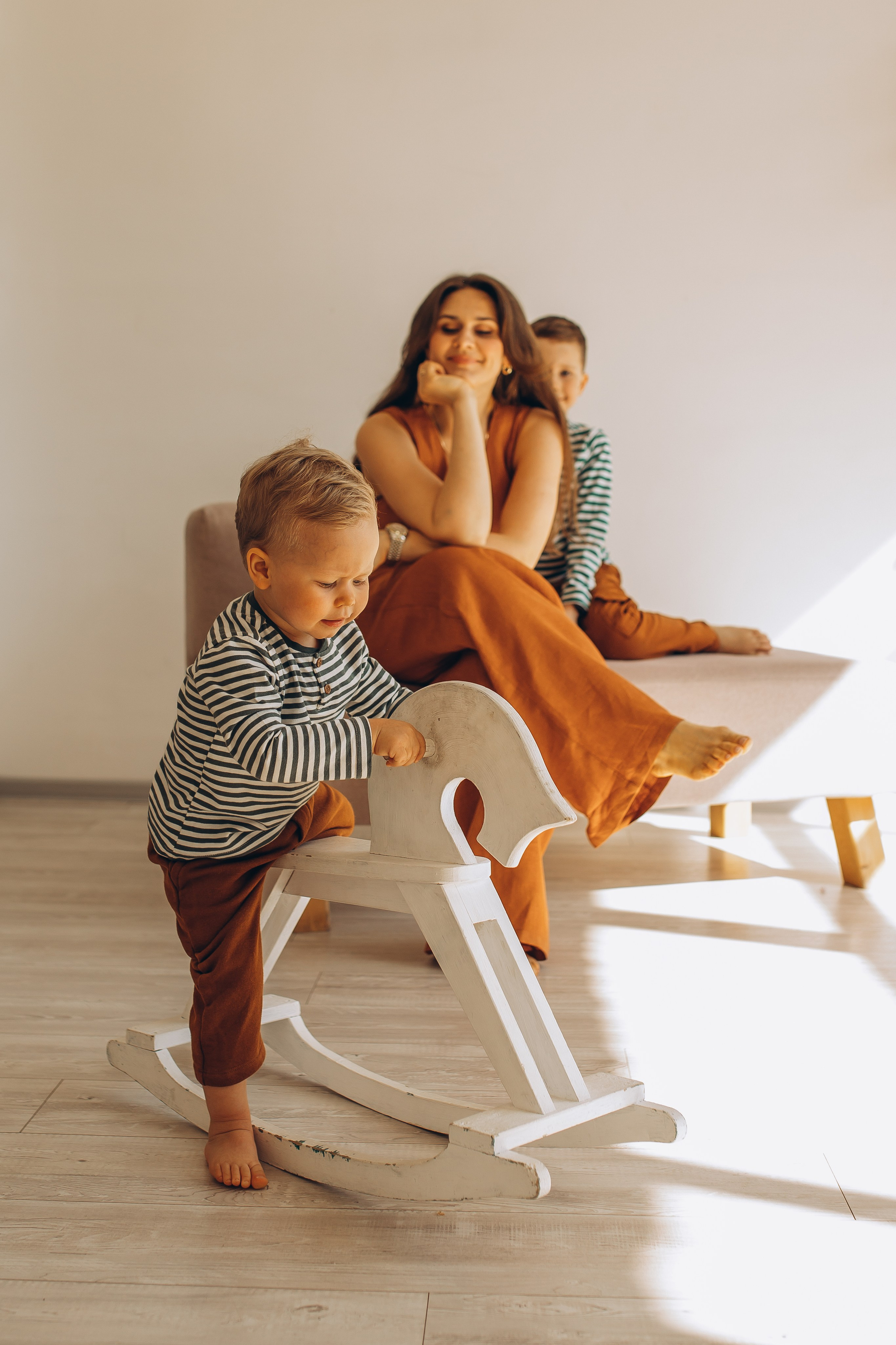 Счастливая мама в оранжевом комбинезоне на фотосессии с сыновьями в светлом интерьере. Детский и семейный фотограф Маруся Самылкина в Санкт-Петербурге.