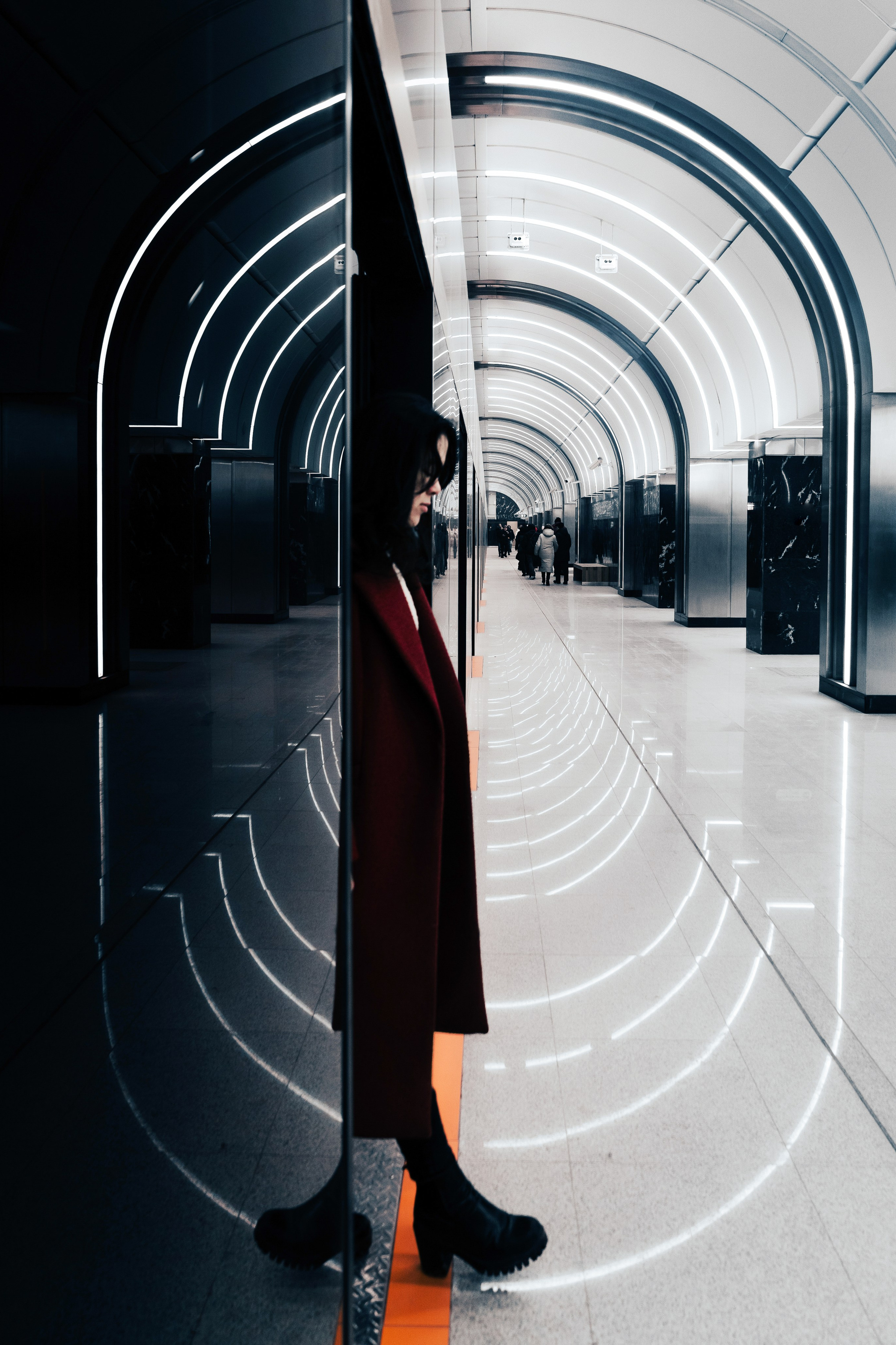 Женщина в красном пальто в футуристическом тоннеле метро с отражениями неоновых линий. Стрит-фотография Мальцева Евгения.