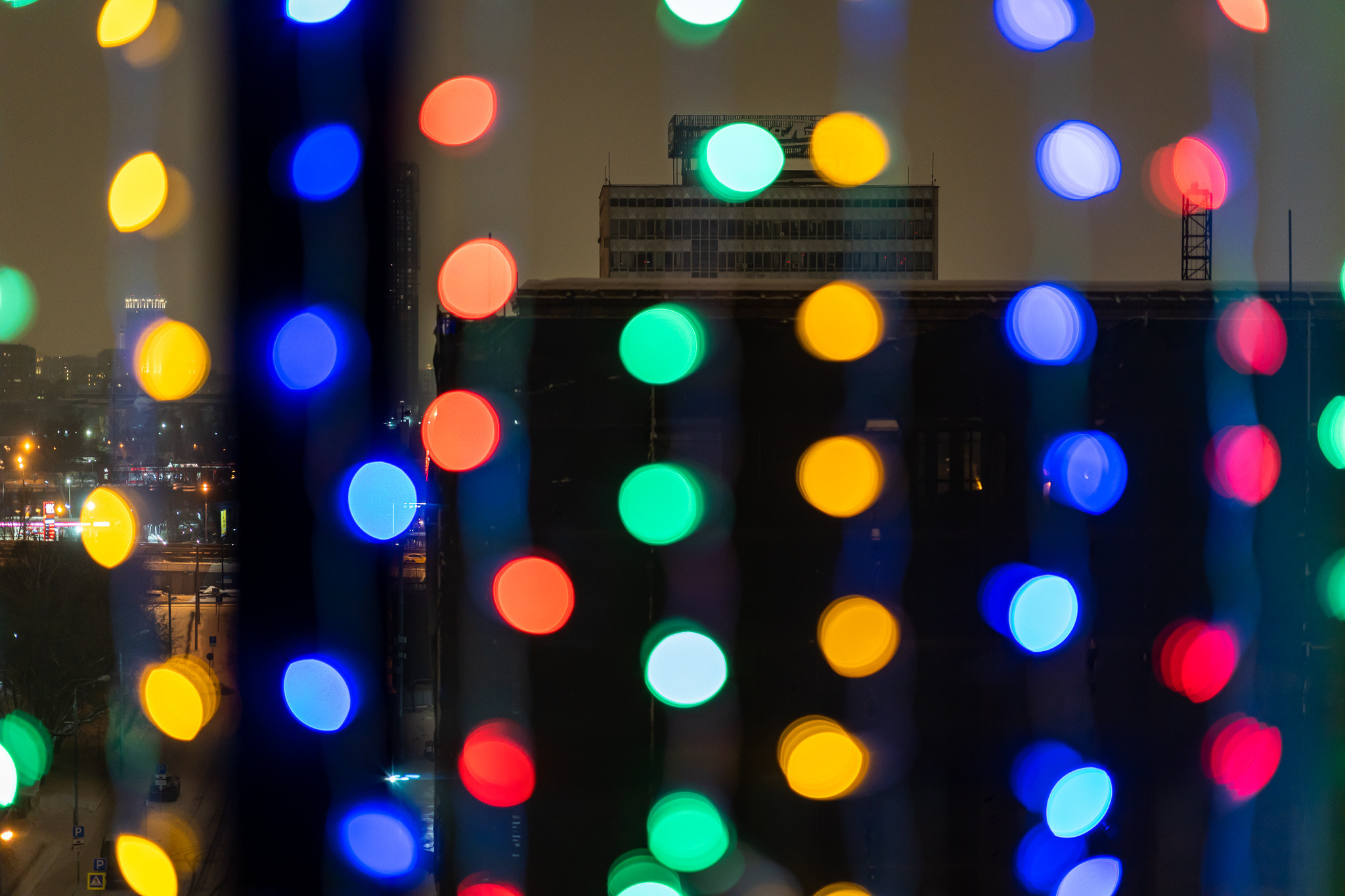 Вид на улицу через окно с разноцветной новогодней гирляндой