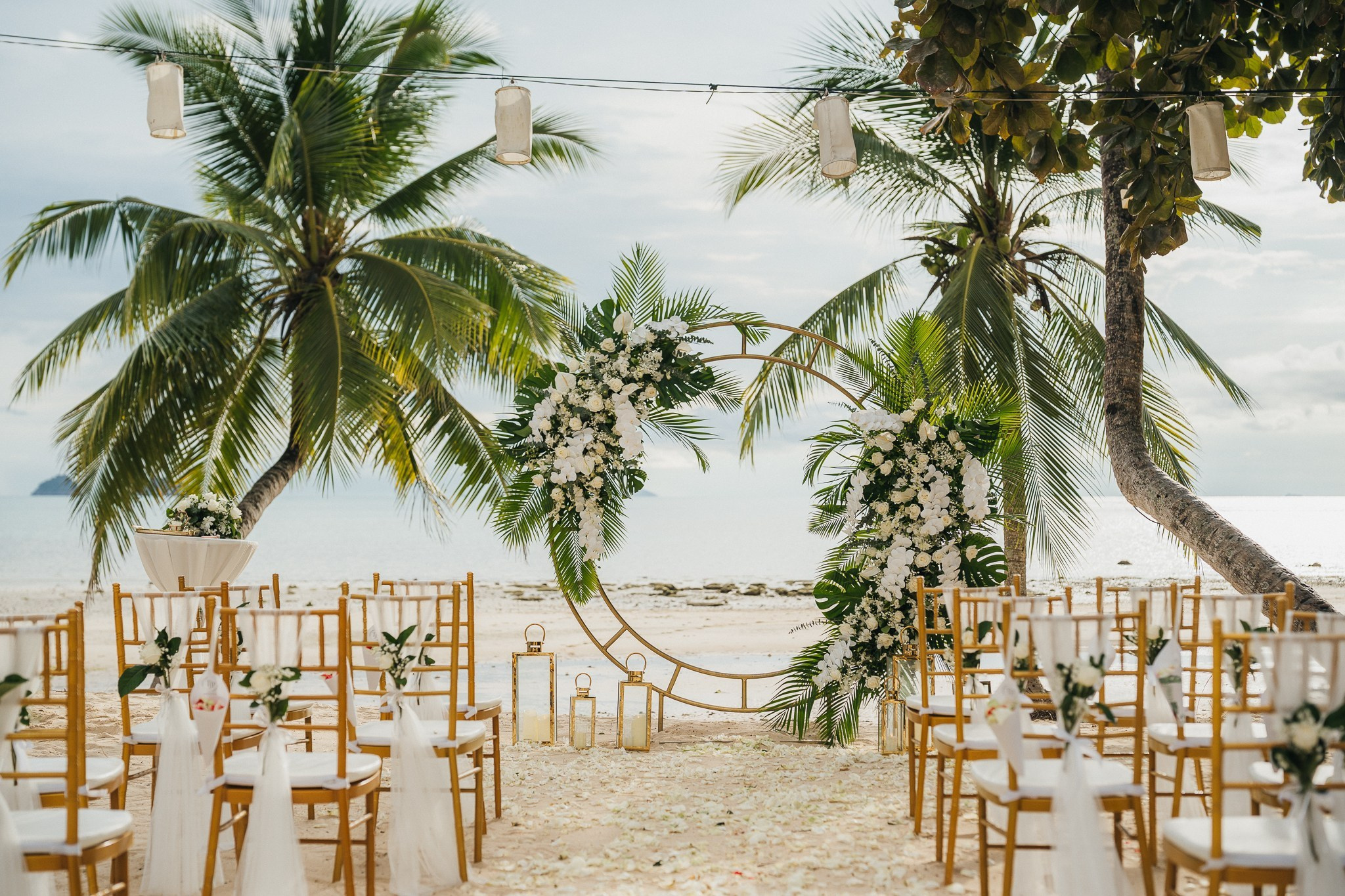 Beach wedding ceremony setup on Koh Samui with a floral arch, wooden chairs, and tropical palm trees overlooking the sea.