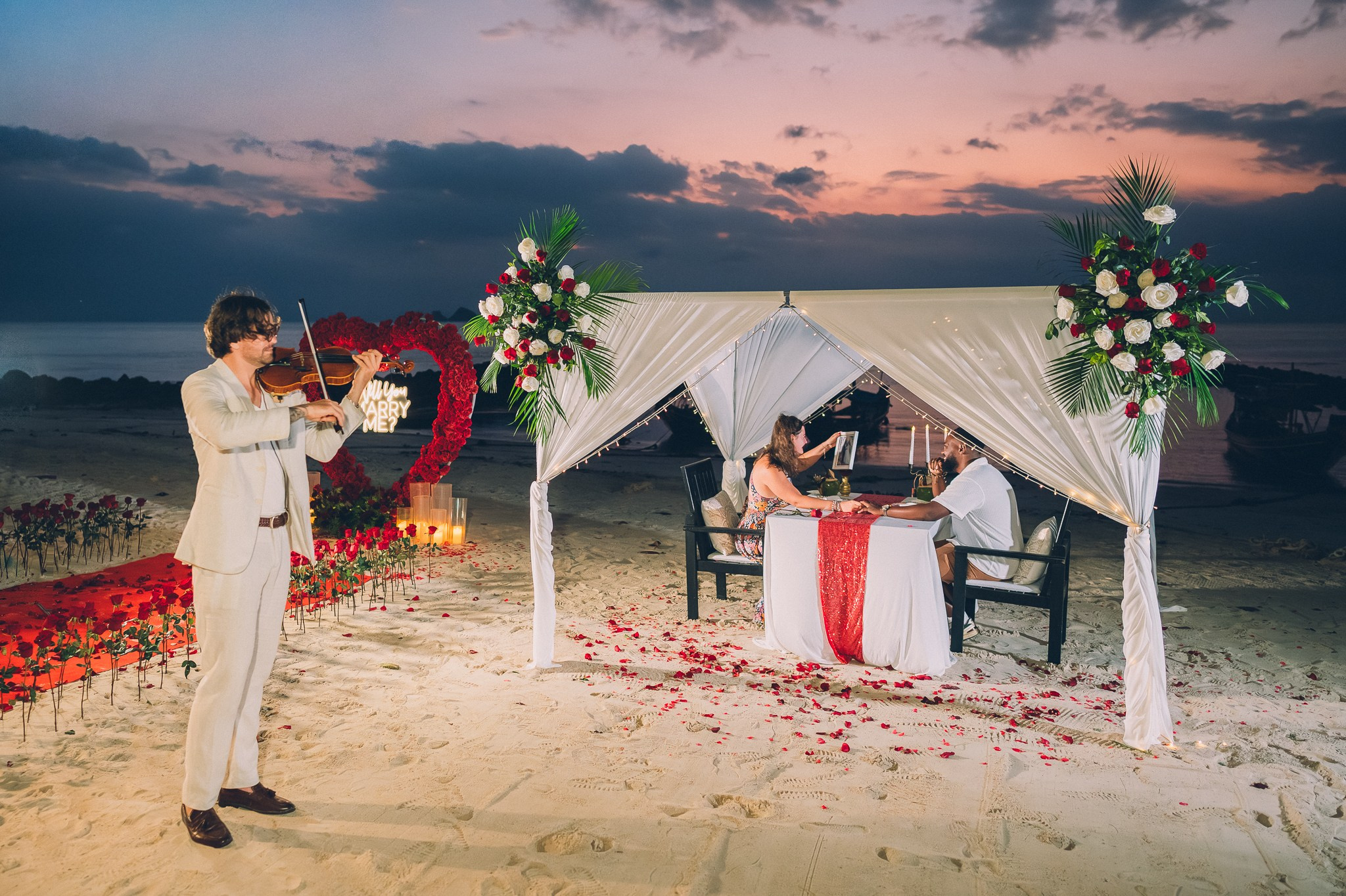 Romantic beach proposal dinner in Koh Samui at sunset with a private table, tropical flowers and a professional photographer capturing the moment.