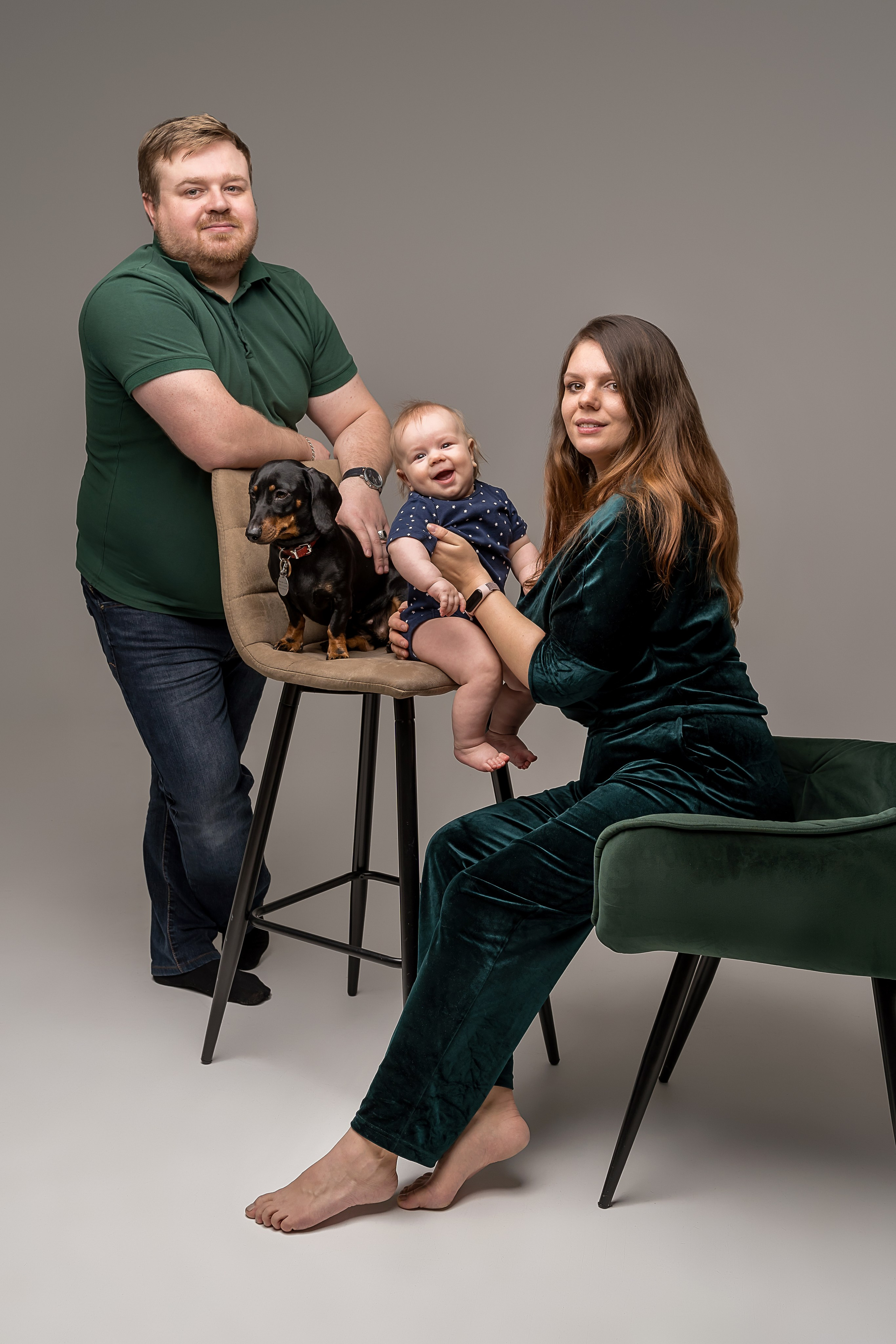 Мама, папа, младенец и собака на сером фоне в фотостудии на циклораме в зелёной одежде. 
