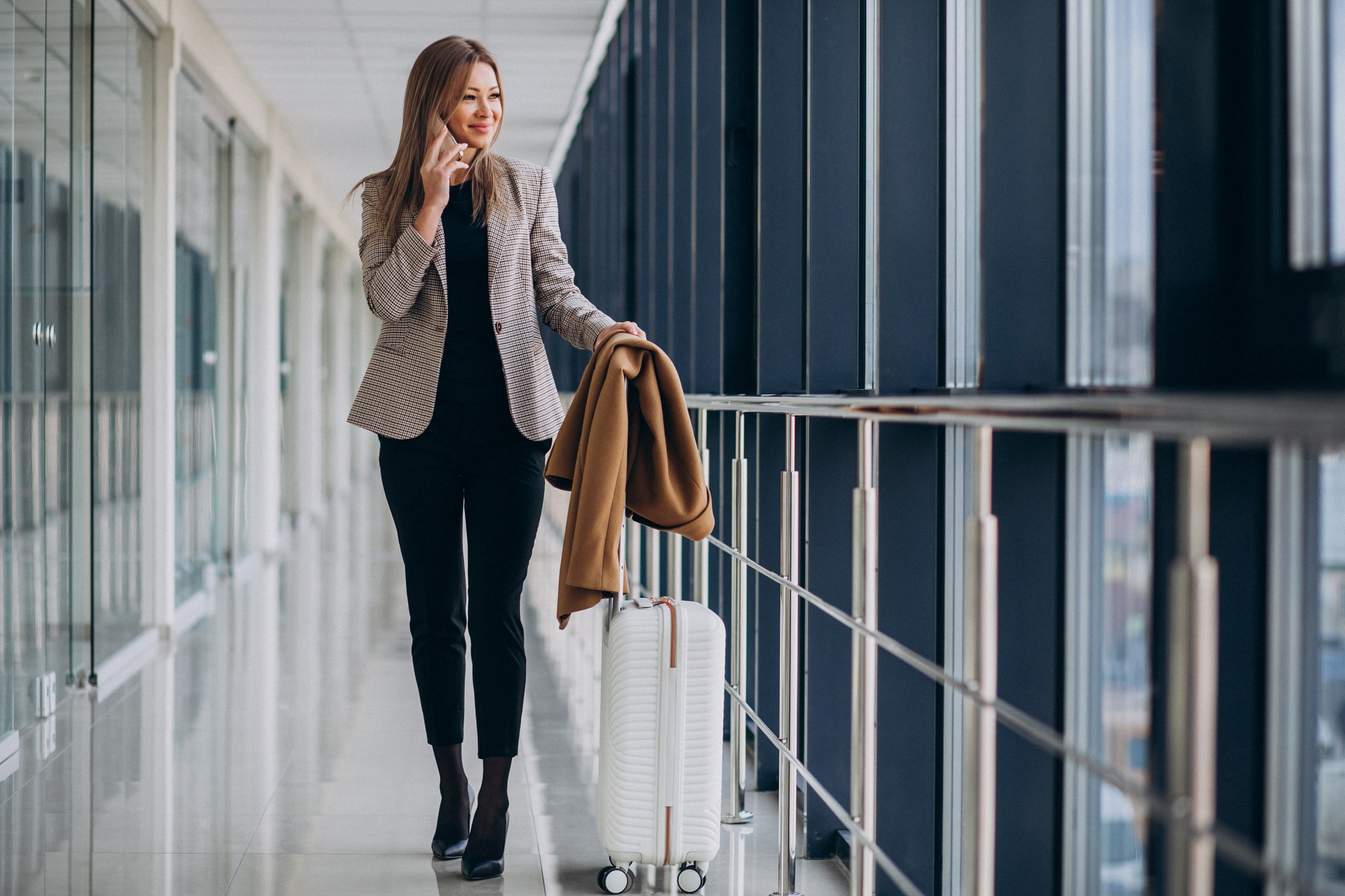 Businesswoman on a call in a corporate travel corridor, luggage in hand — Supreme Travel corporate travel services