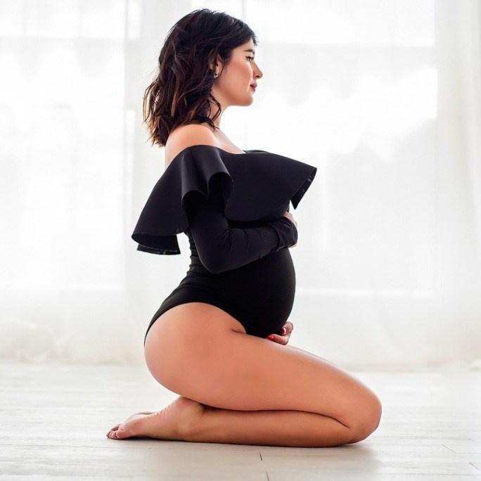 Беременная женщина в черном боди с воланами на плечах фотосессия беременности