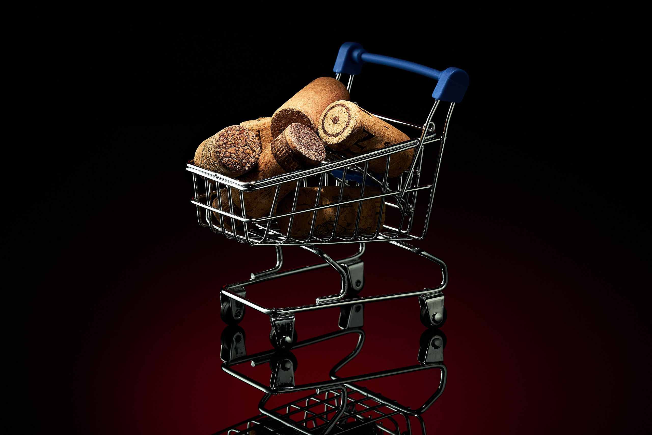 Миниатюрная тележка супермаркета с винными пробками на чёрно-красном фоне, художественная предметная фотография