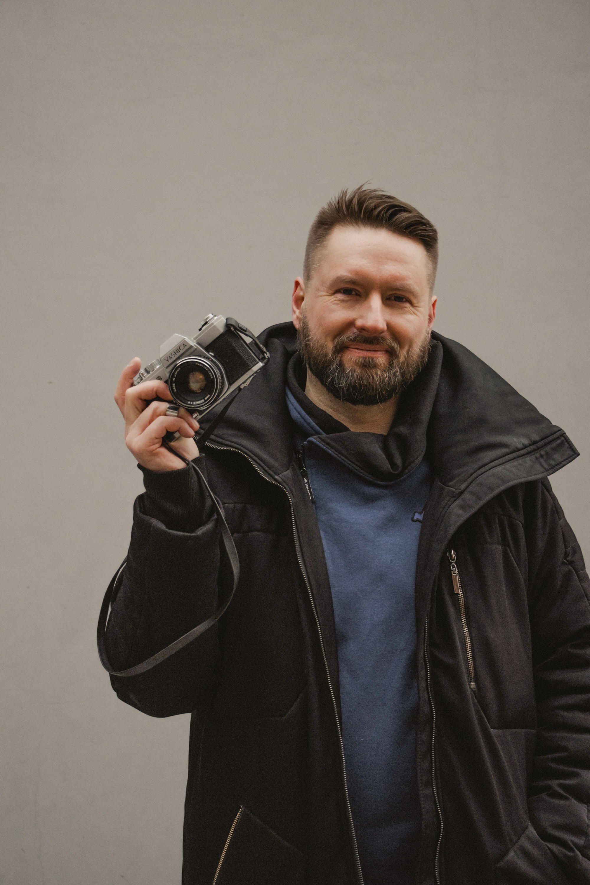 Виктор Кудряшов, фотограф держит в одной руке фотоаппарат, улыбается.