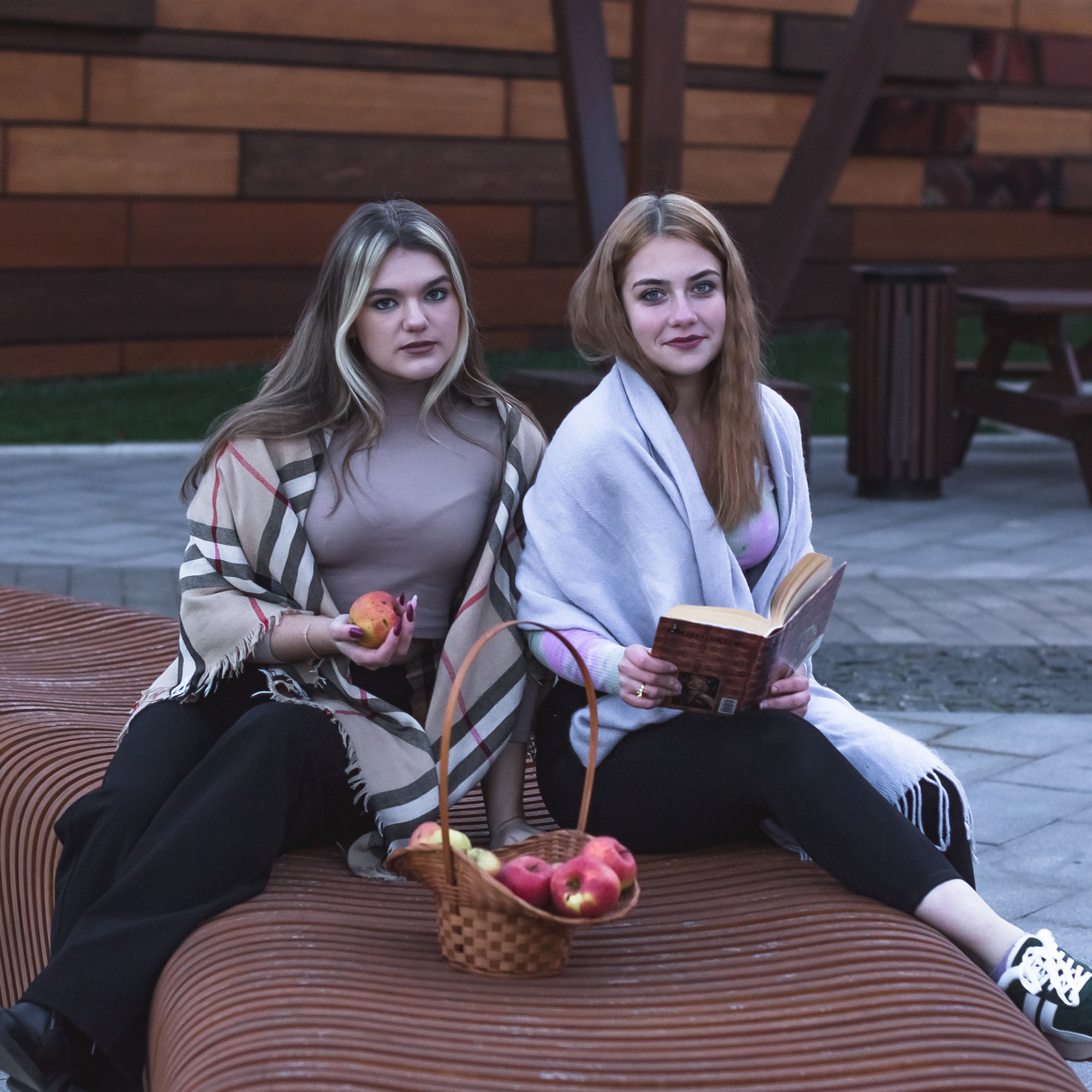 На фотографии две девушки с яблоками  сидят рядом и улыбаются.