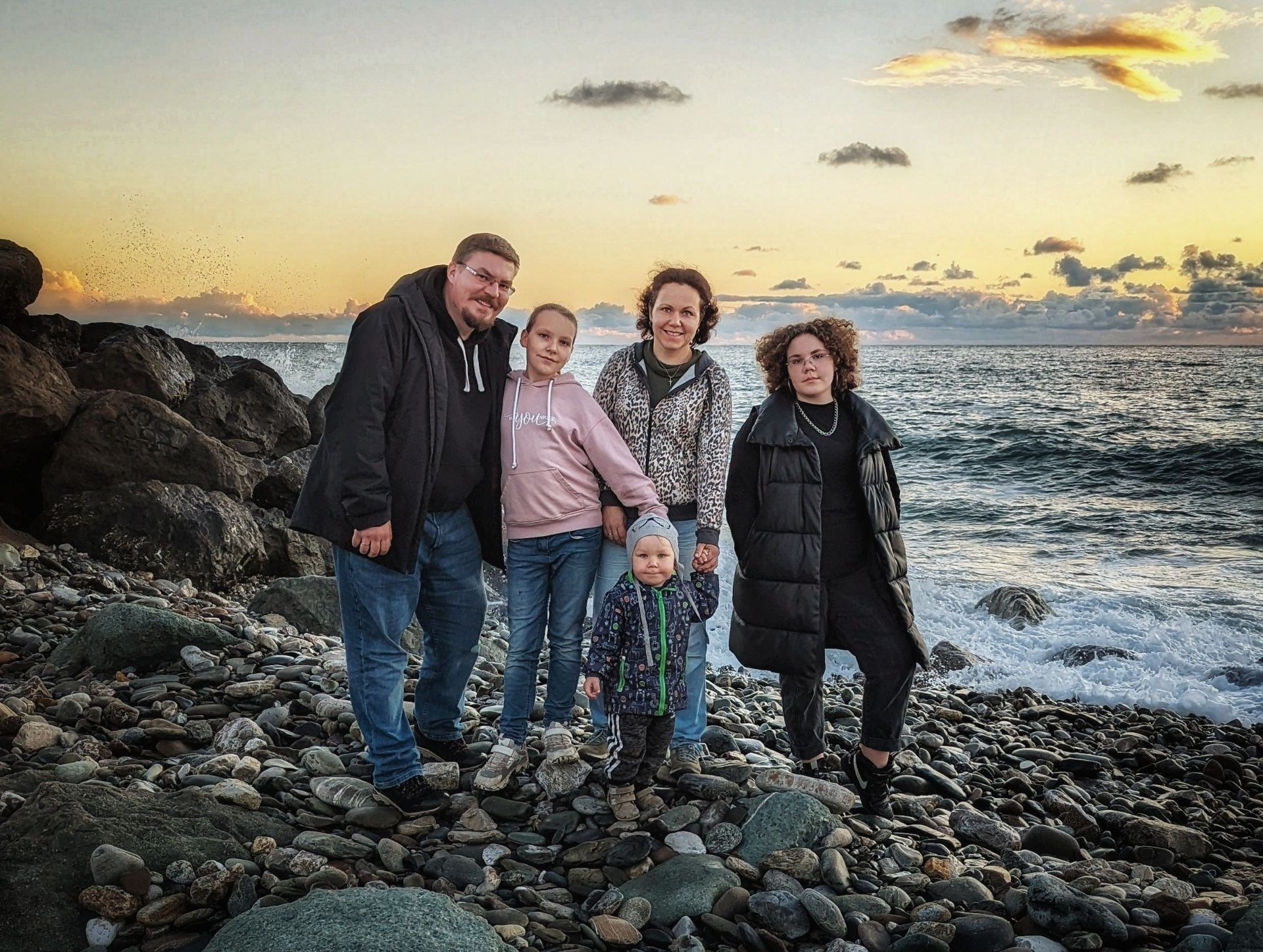 Семья из пяти человек на закате на галечном пляже у моря