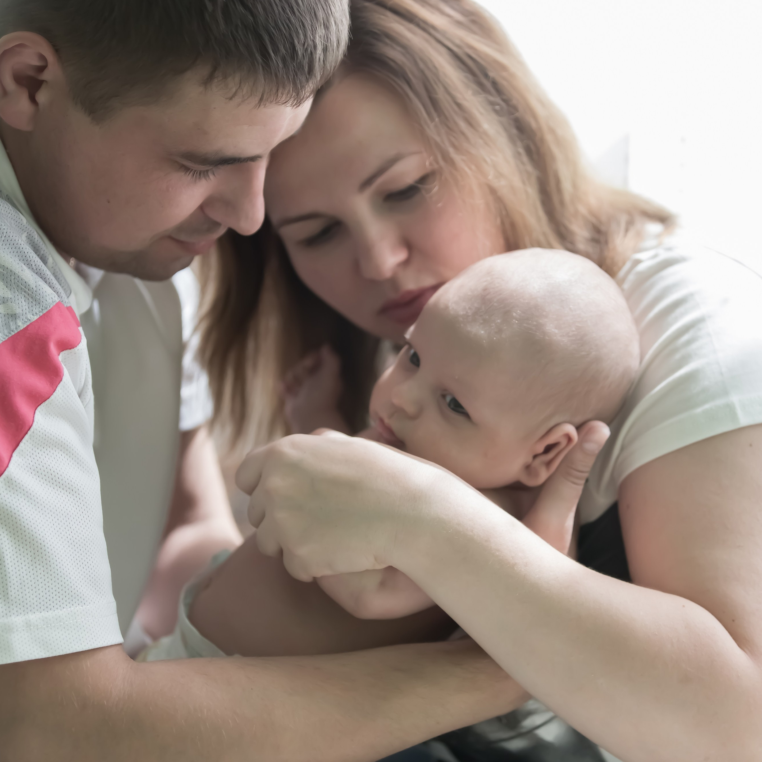 папа и мама держат на руках своё дитя возрастом до 1 месяца, смотрят с любовью и заботой