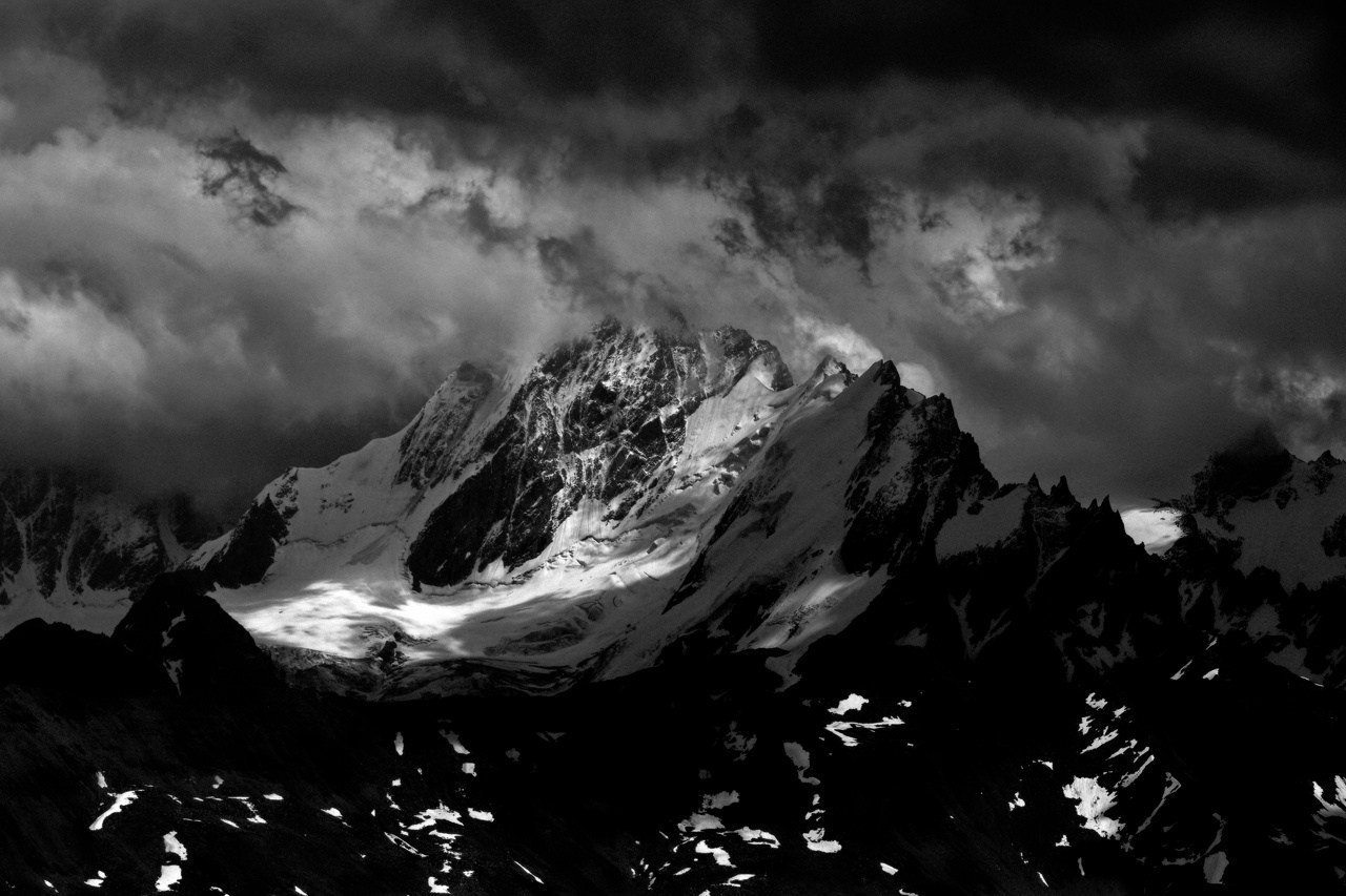 Снежная горная вершина в драматичных облаках, контрастная черно-белая фотография горного пейзажа