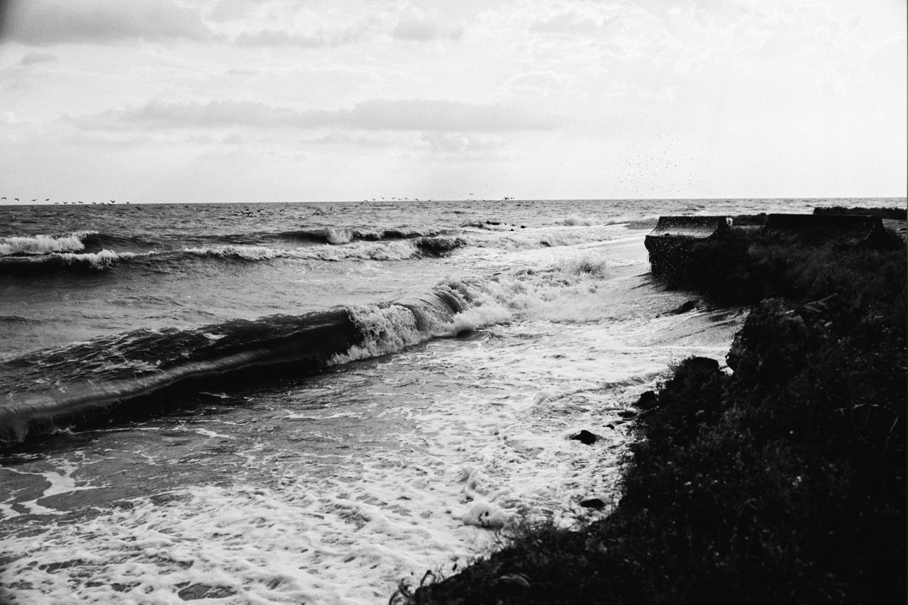 Волны разбиваются о бетонные укрепления берега, динамичная черно-белая фотография моря с эффектом смазанности