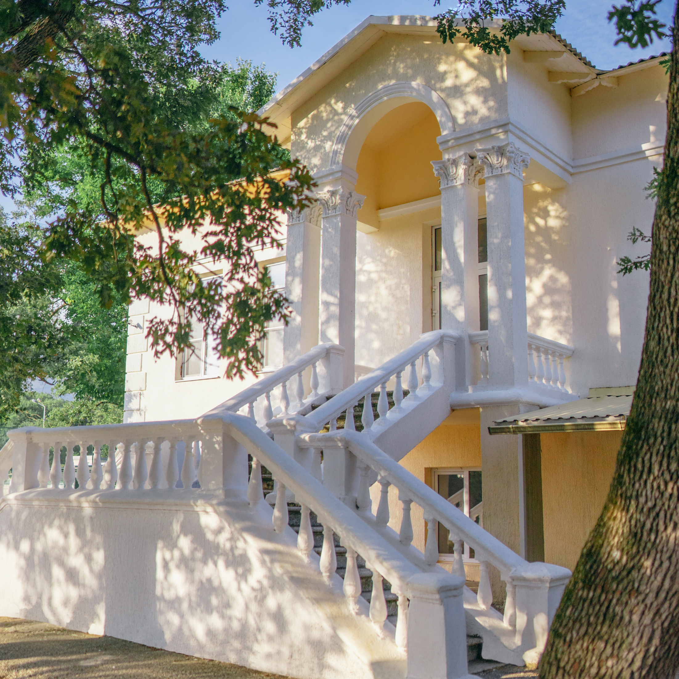 Главный корпус детского лагеря Альбатрос, находящегося в Кабардинке. Здание утопает в зелени, красивый солнечный свет.