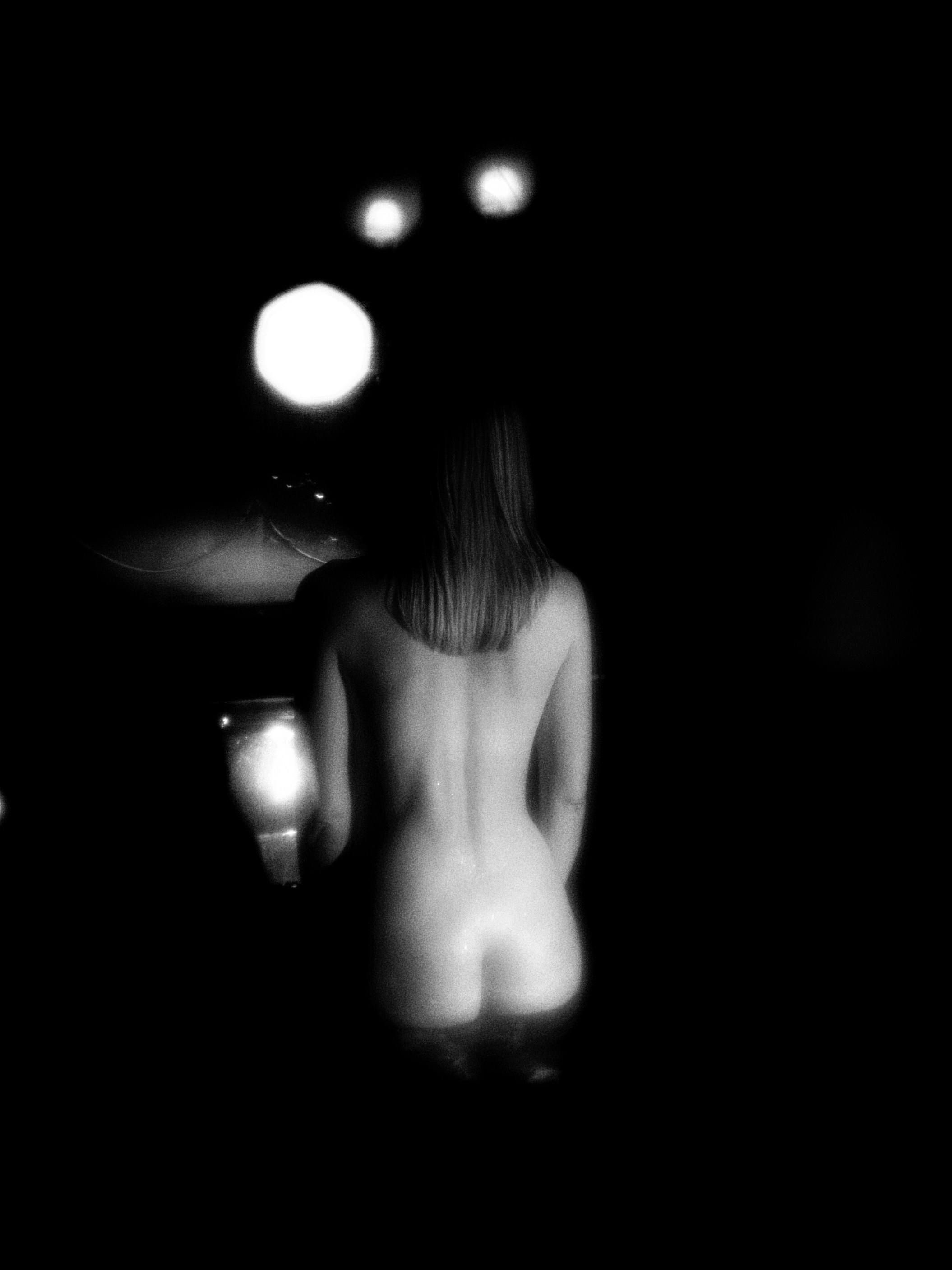 Обнаженная девушка сидит в ванной в полной темноте.