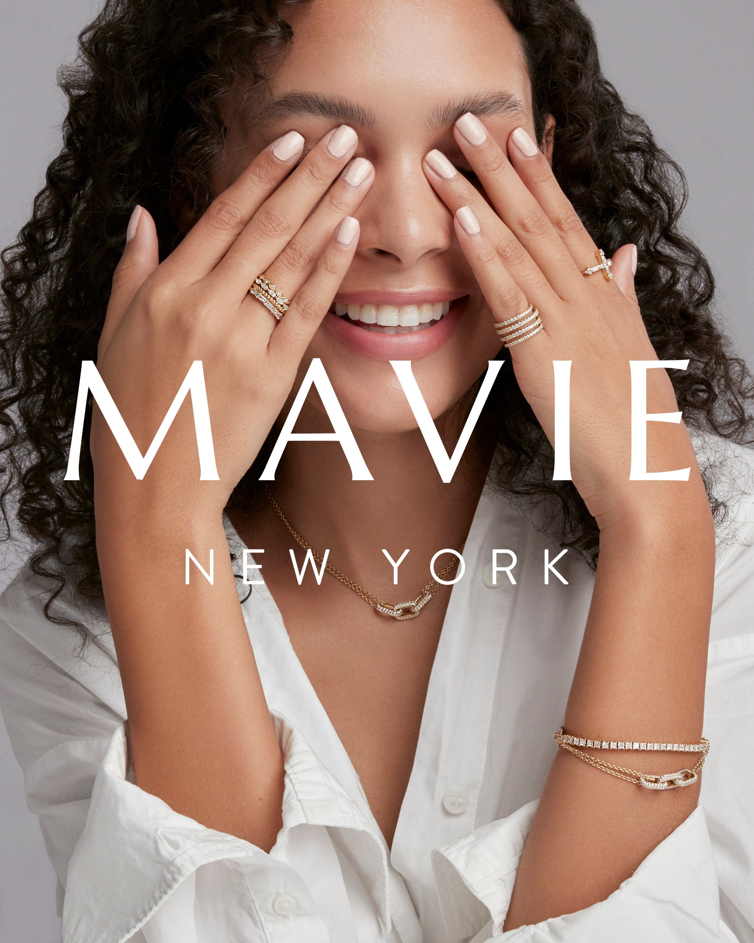 Smiling model covering her face with hands, featuring delicate jewelry and radiant skin.