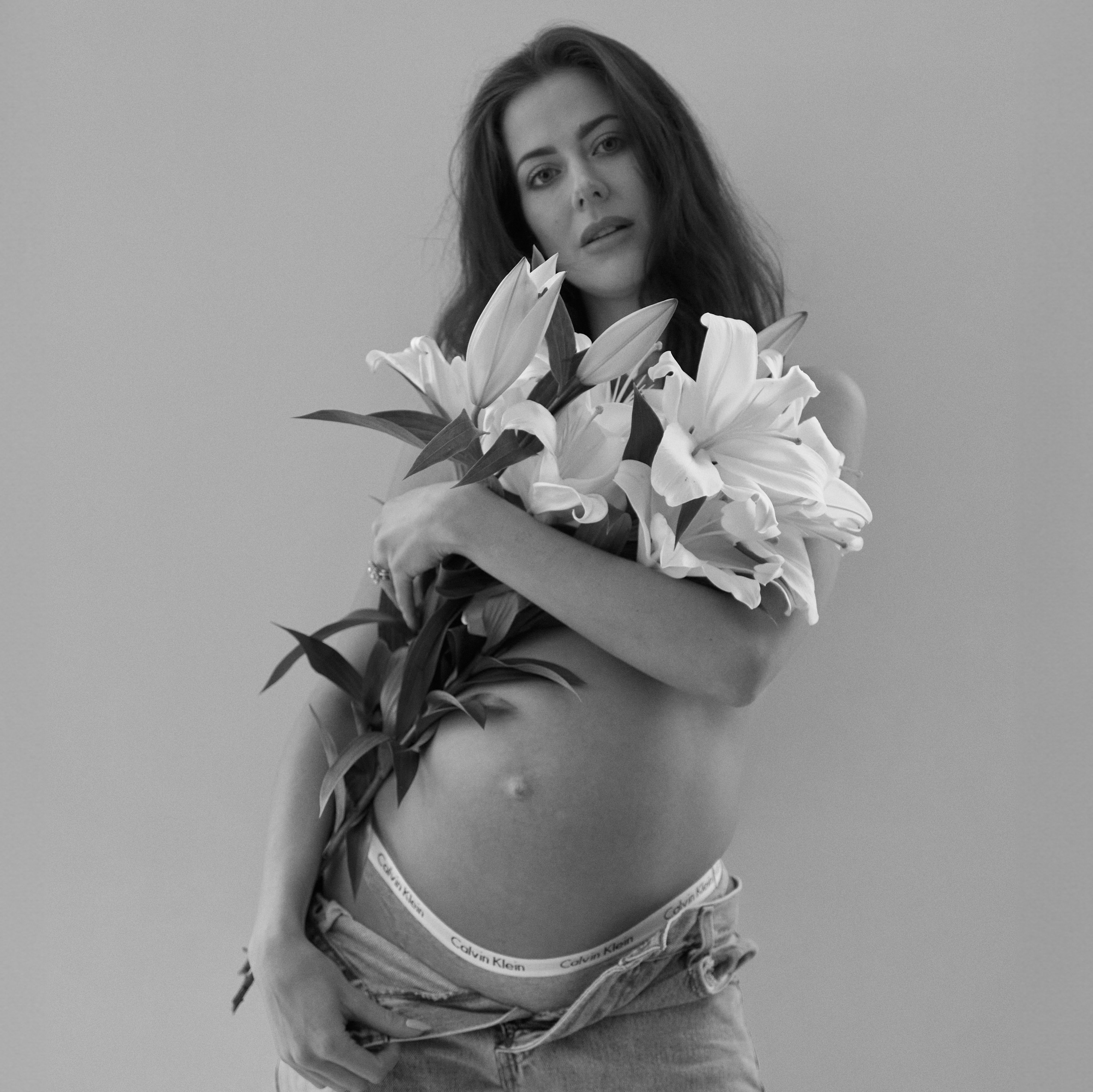 A pregnant woman poses with lilies, highlighting the beauty of best pregnancy photos in a simple and elegant setting