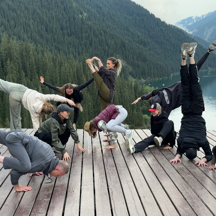 Группа людей, участников корпоративного тура Melon Travel на озеро Иссык, одетых в зимнюю одежду, позирует на фоне заснеженного пейзажа. На земле лежит снег, деревья покрыты инеем, а на заднем плане виднеется туман, создающий атмосферу спокойствия и загадочности. Участники группы улыбаются и выглядят счастливыми.