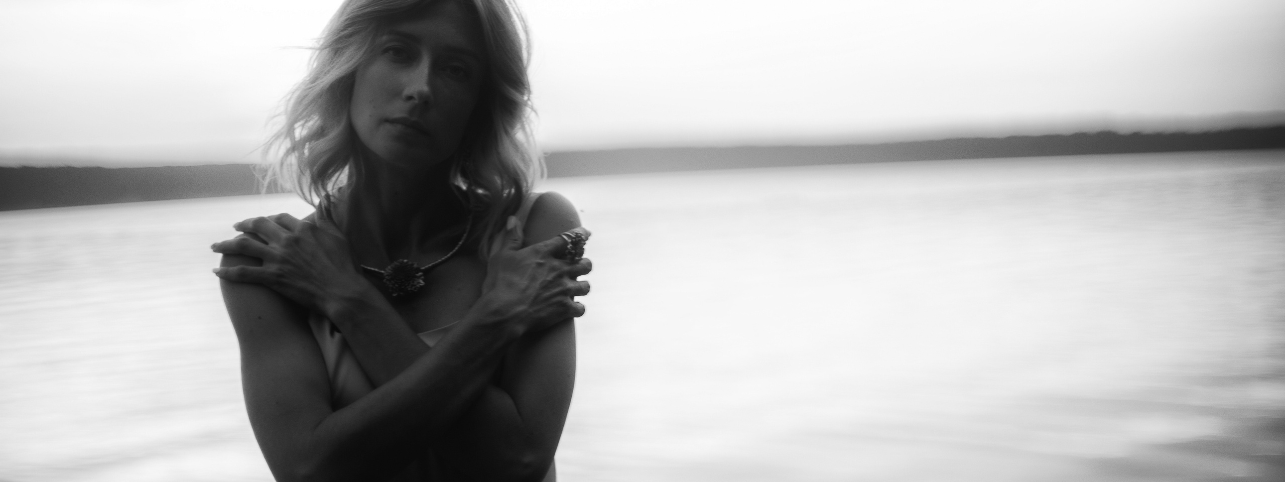 Черно-белый портрет молодой девушки в платье на берегу реки или озера на закате