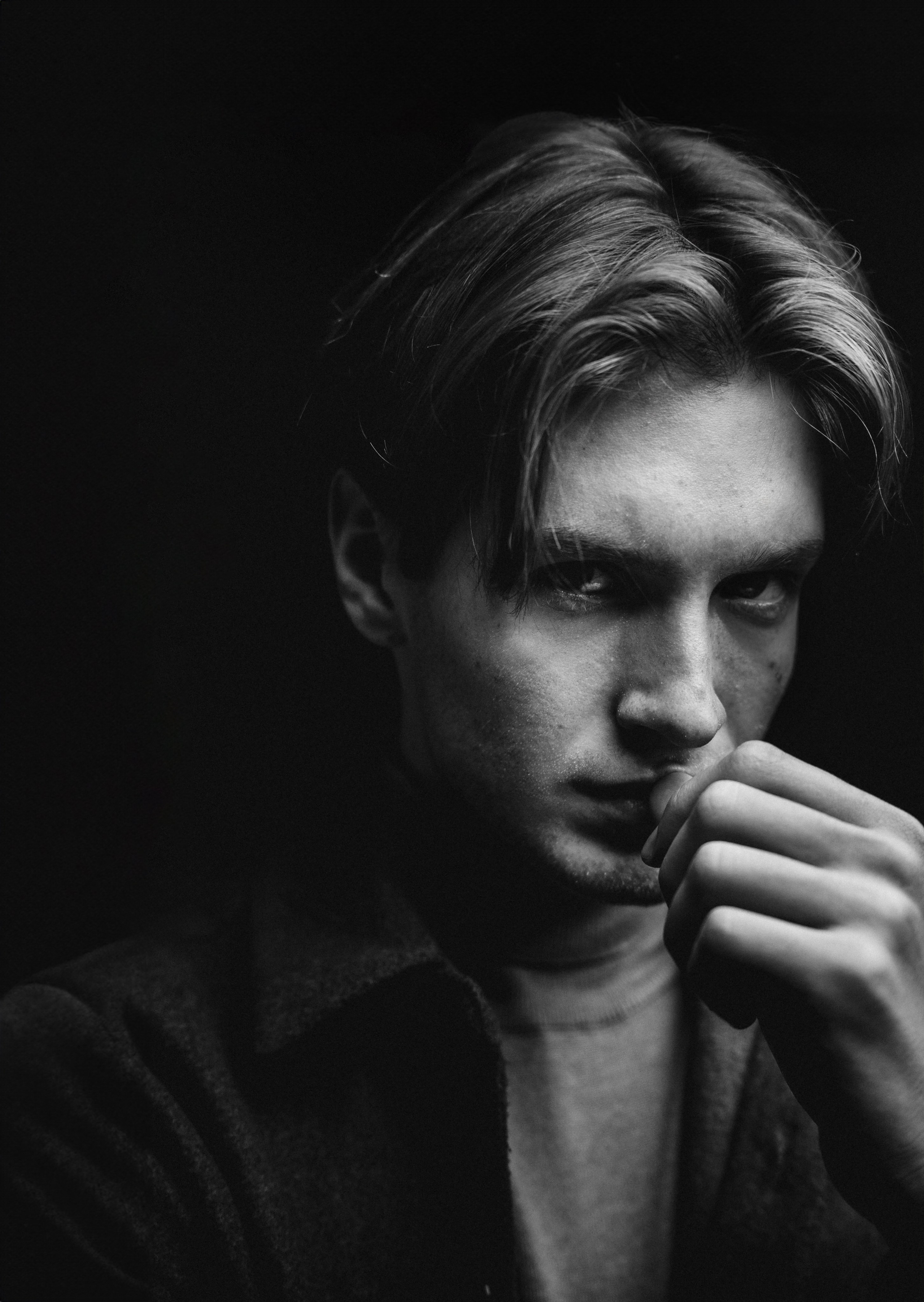 Молодой человек в коричневом пиджаке и оранжевой футболке сидит в студии, спокойно смотрит в сторону в задумчивой позе