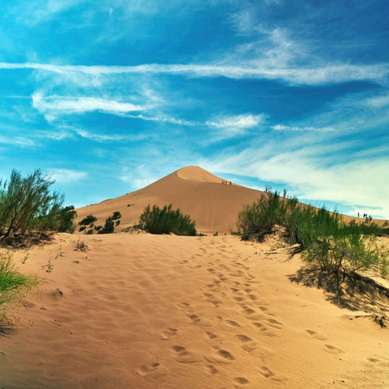 Человек стоит у подножия замерзшего водопада Медвежий среди заснеженных скал. Вода продолжает течь, частично покрытая льдом, создавая красивый контраст между движущейся водой и ледяными наростами. Земля вокруг покрыта снегом, создавая зимнюю атмосферу. Человек одет в теплую одежду — синее пальто с капюшоном и розовую шапку.