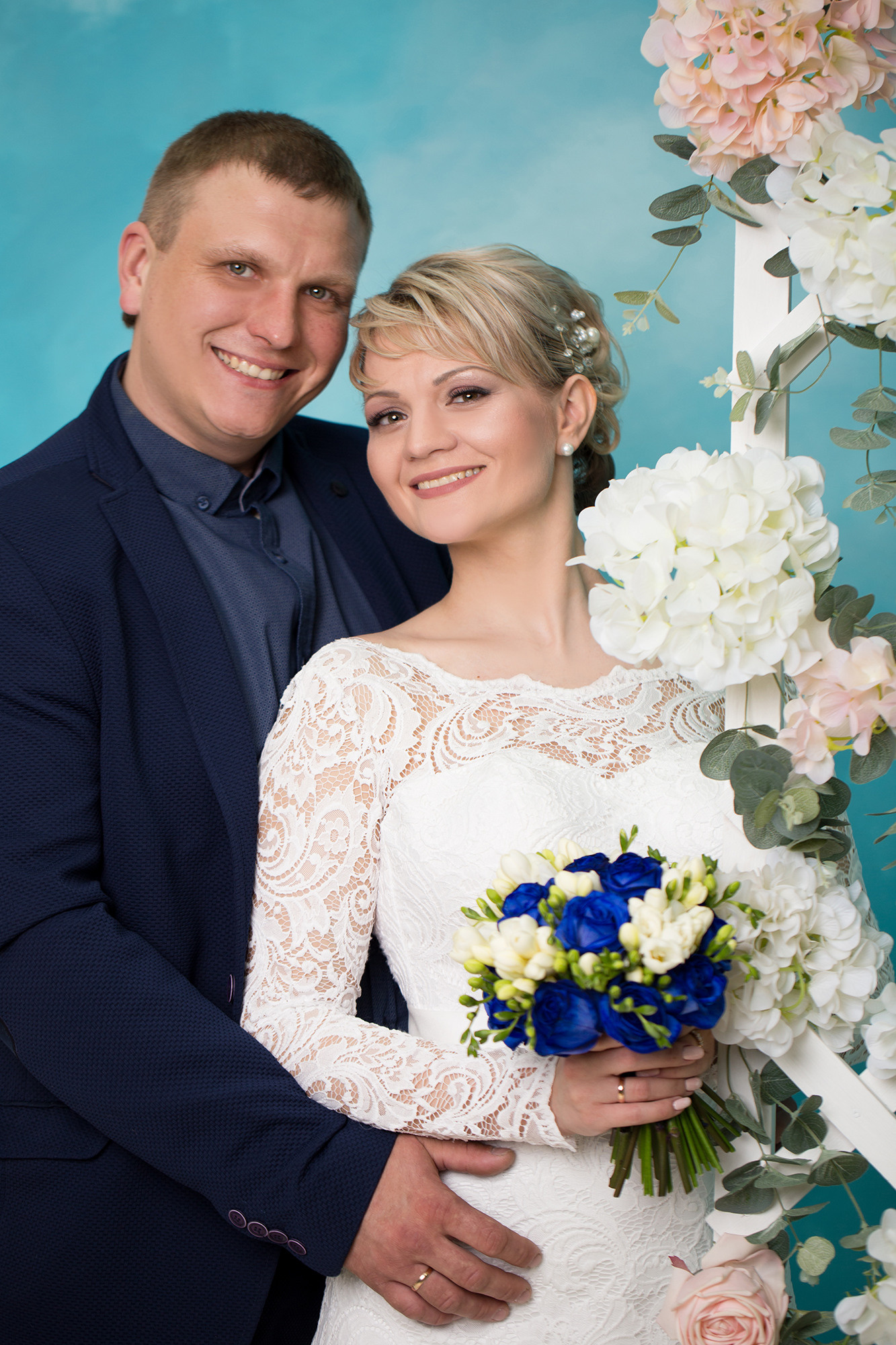 жених обнимает невесту с букетом цветов на голубом фоне