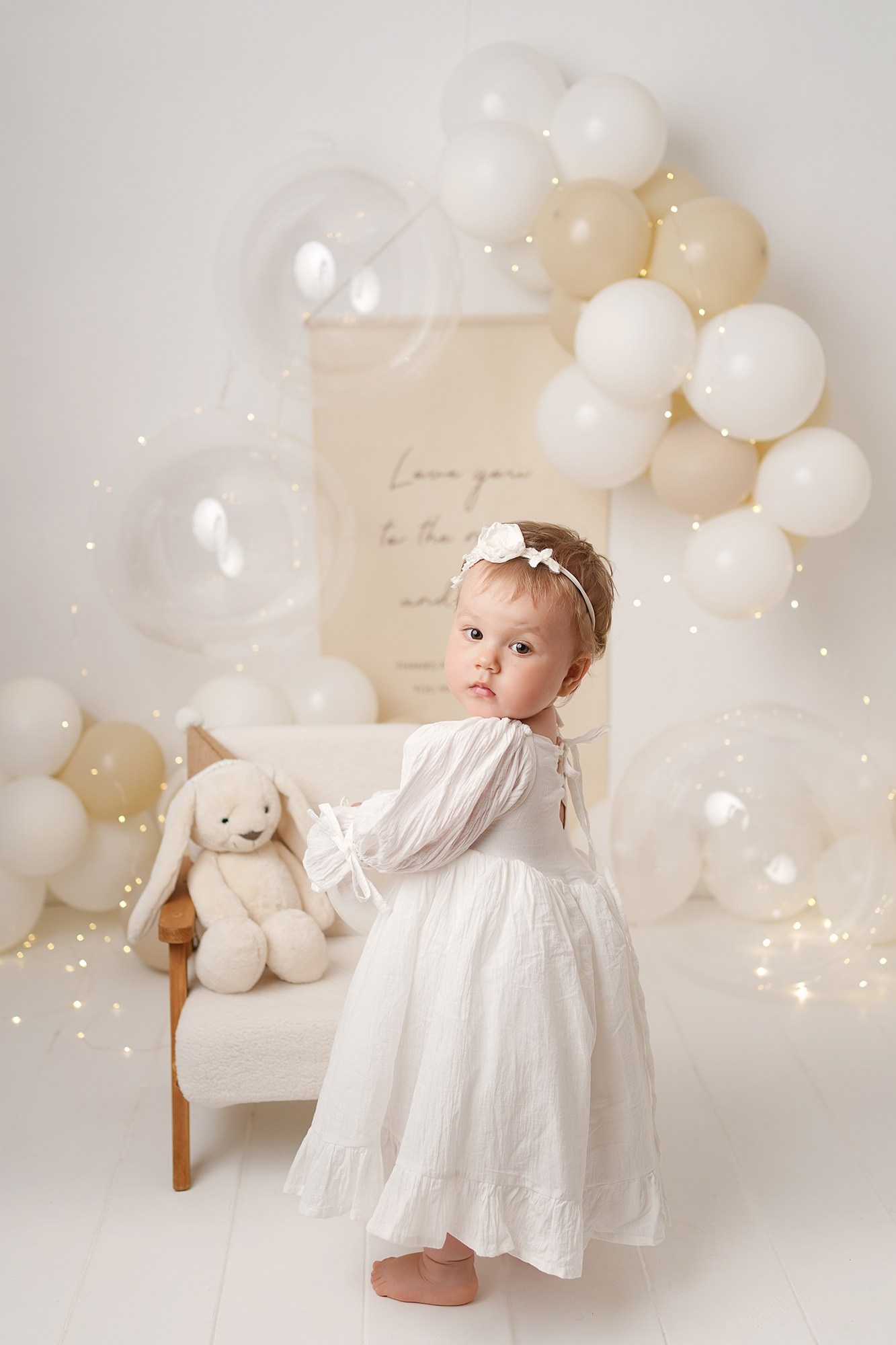 Семья приехала на фотосессию. На фото малышка с игрушкой зайки. Вокруг белые и бежевые шарики.