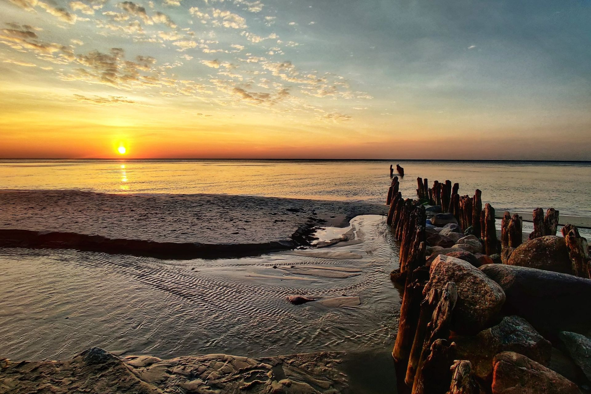 Закат над Балтийским морем с деревянными сваями и камнями на берегу