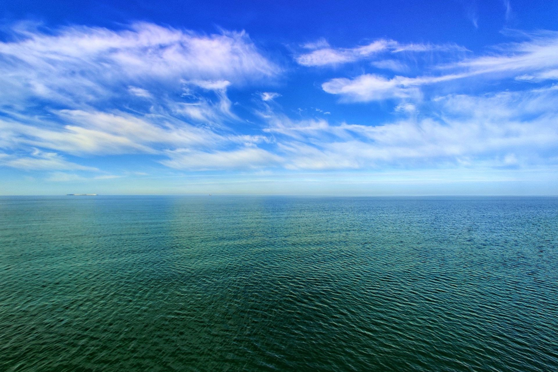 Безмятежная гладь моря под ярко‑синим небом с лёгкими облаками, уходящая за горизонт в солнечный ясный день