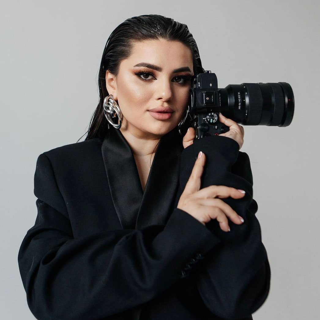 Брюнетка в чёрном костюме с фотоаппаратом