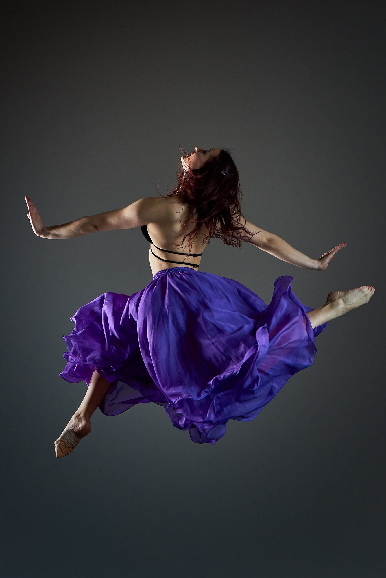 Танцовщица в фиолетовом платье выполняет стремительный вращающийся прыжок, подчёркивающий динамику ткани и выразительную пластику. Художественная съёмка в атмосфере высокой моды. Автор: Александр Шадрин, Москва, Истринский район.