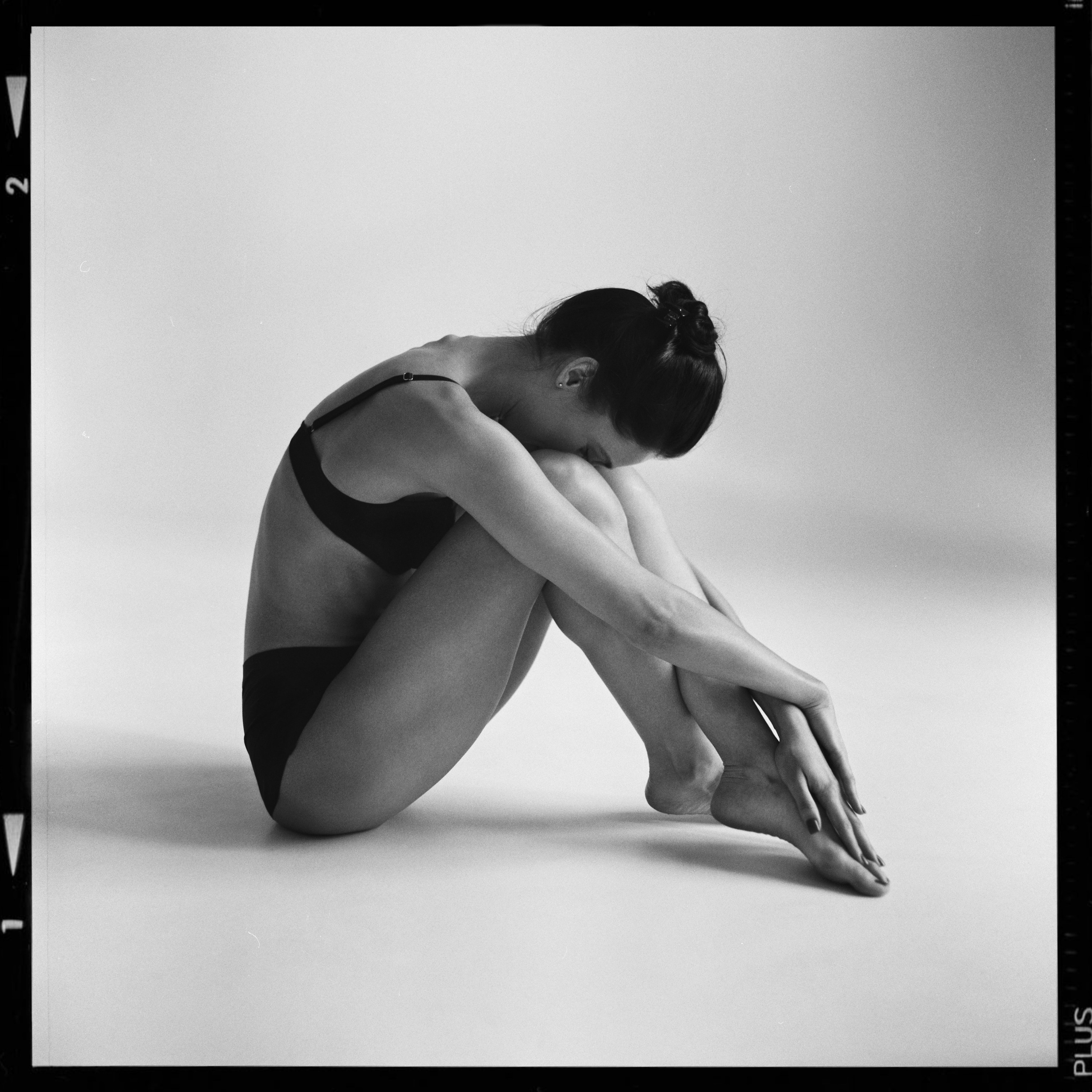 Артистка балета сидит на белой циклораме в черном белье