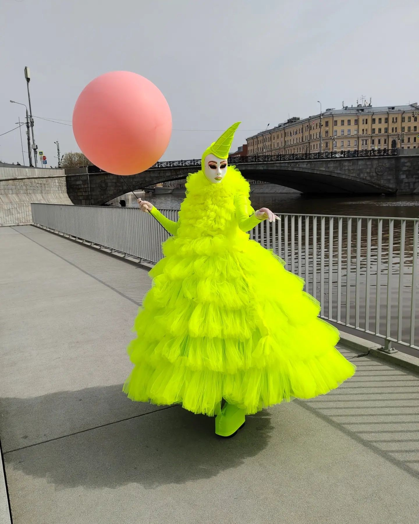 Мим в лимонном костюме стоит на набережной реки Москвы и держит в руках большой красный шарик