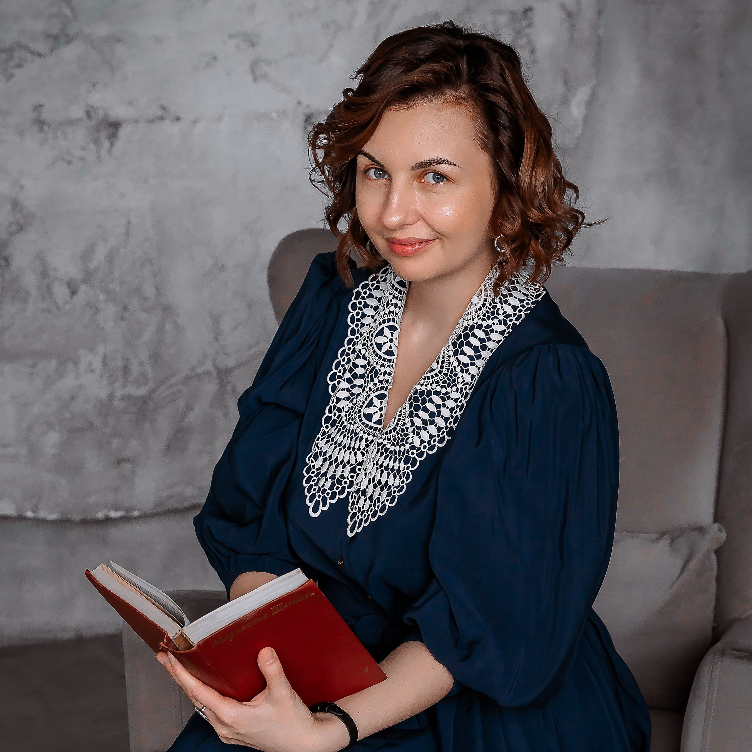 Классный руководитель в синем бархатном платье сидит на кресле.